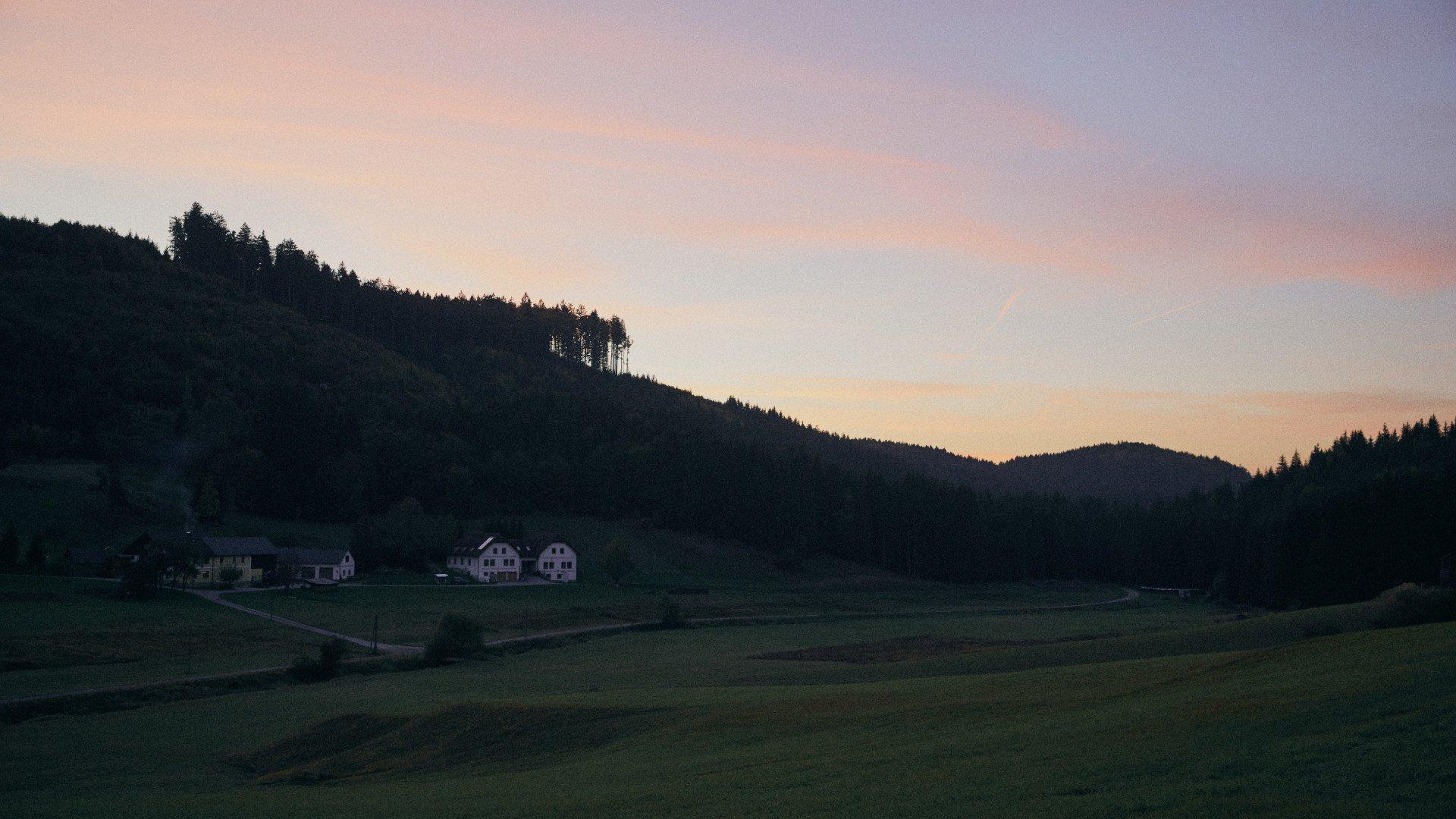 Rural landscape with houses nestled in valley between forested hills at dusk with pink and purple sky