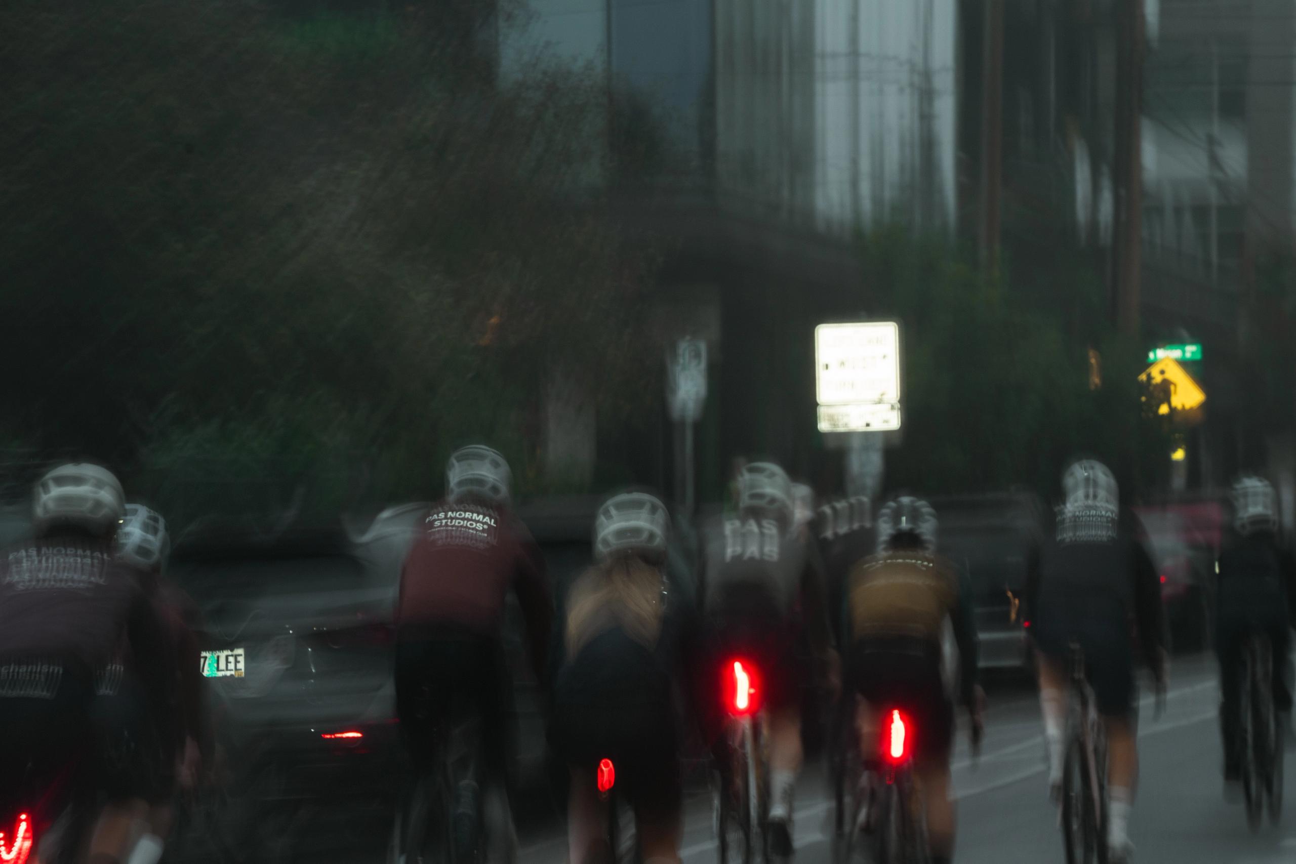 Group of cyclists riding in wet conditions with motion blur and red tail lights visible