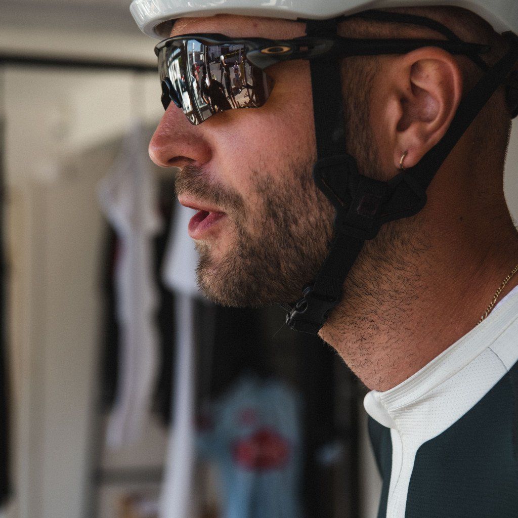 Model wearing white helmet and mirrored sunglasses with dark cycling jersey and white collar detail