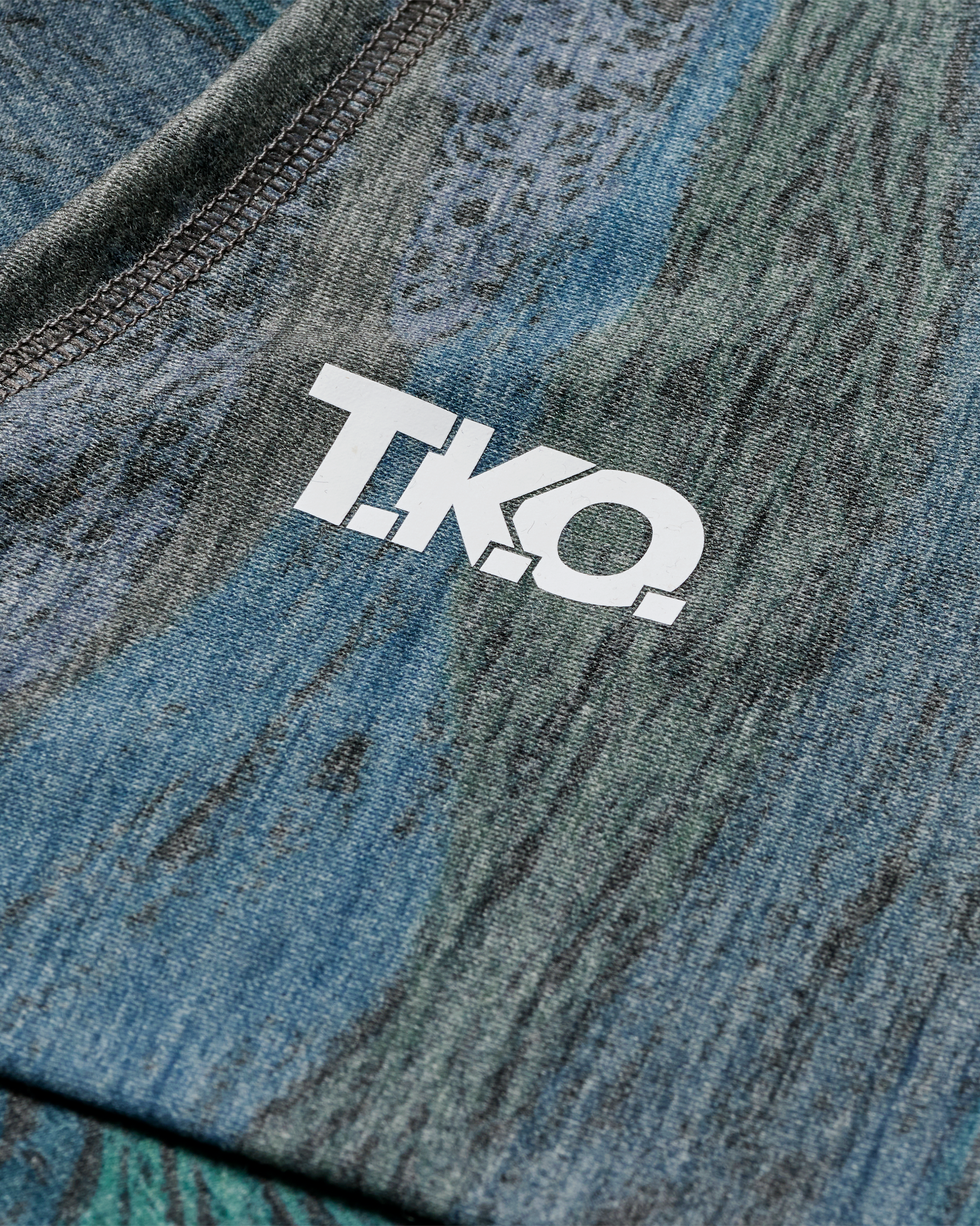 Dark Multi T.K.O. Merino necktube, detail view with white T.K.O. logo print on textured blue-green pattern