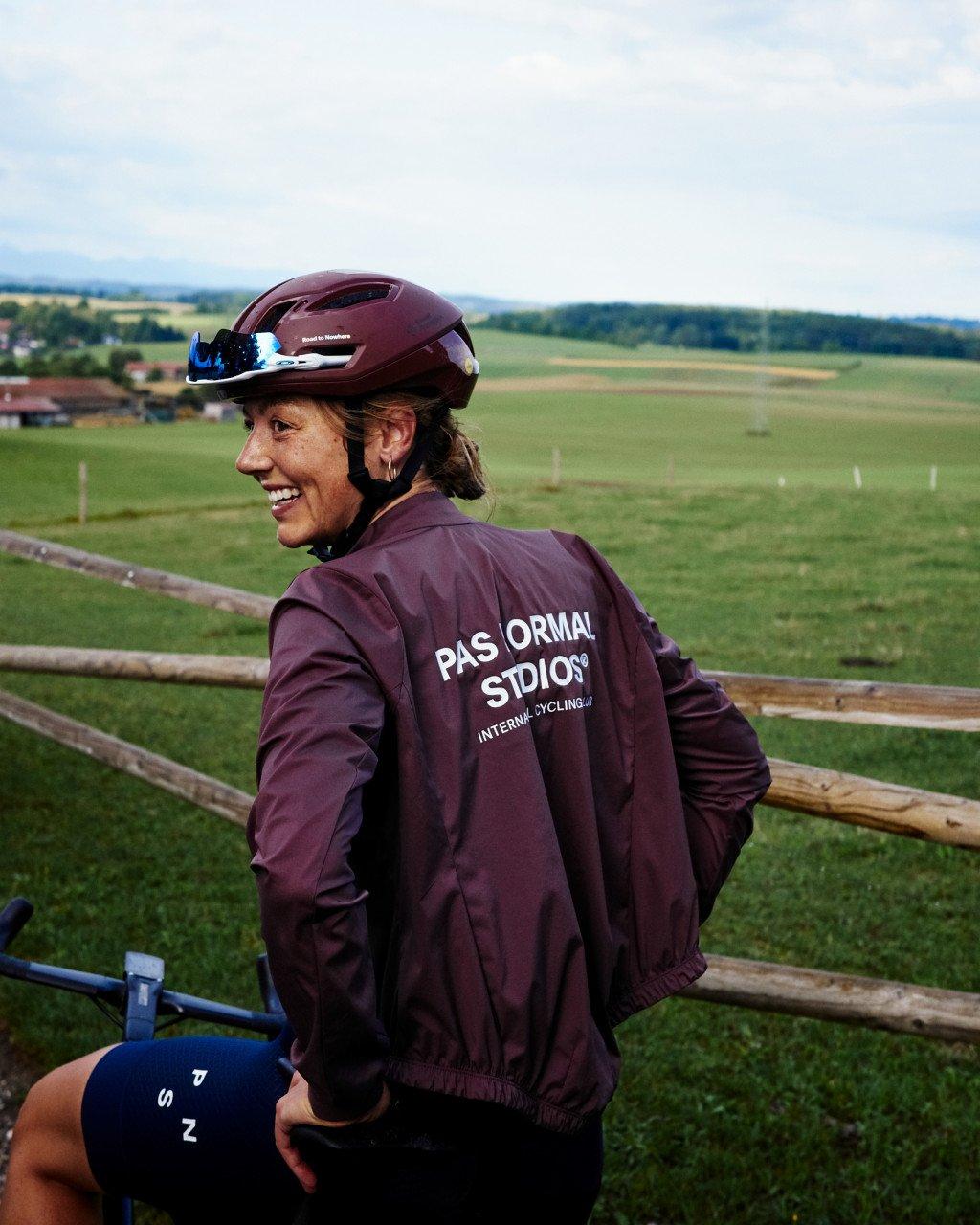 Model wearing burgundy cycling jacket with back branding in countryside setting