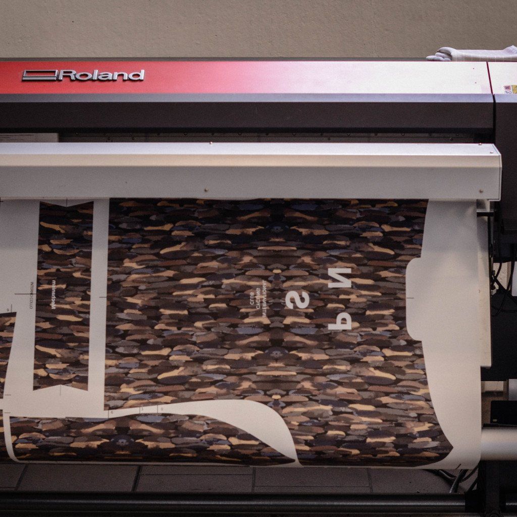 Large format printer producing brown camouflage pattern fabric with white branding text