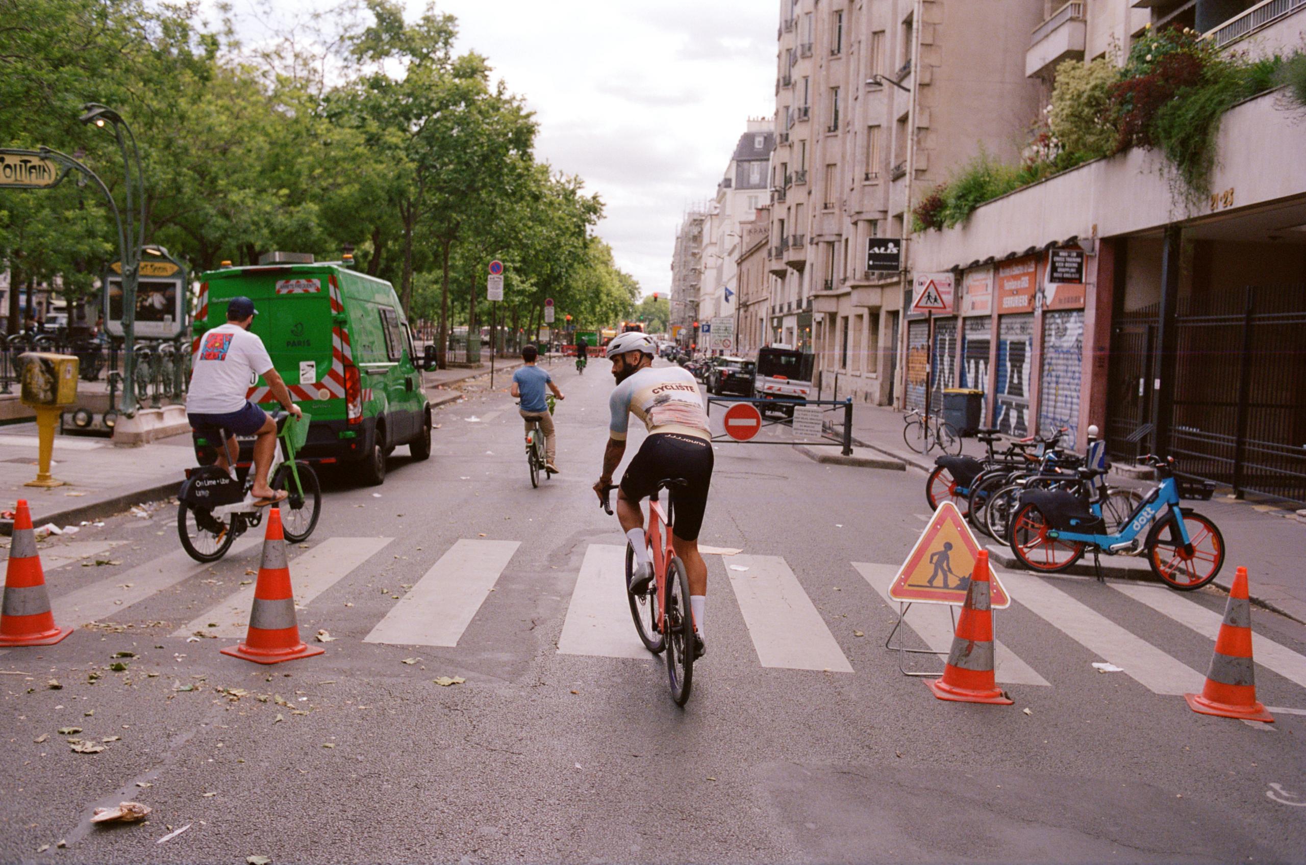 Model wearing white jersey cycling through Paris street with traffic cones