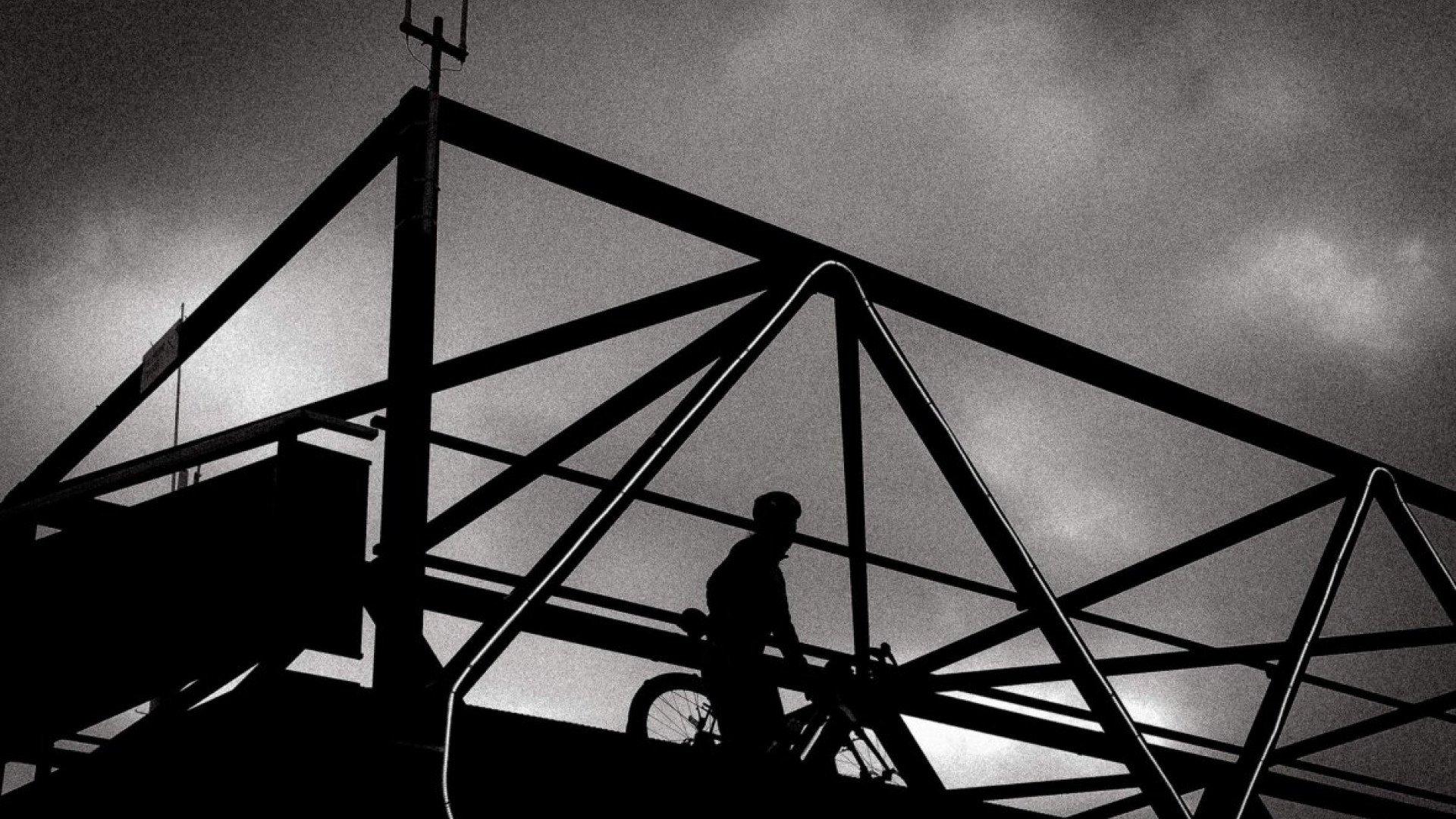 Cyclist silhouette on bridge with dramatic steel framework against cloudy sky