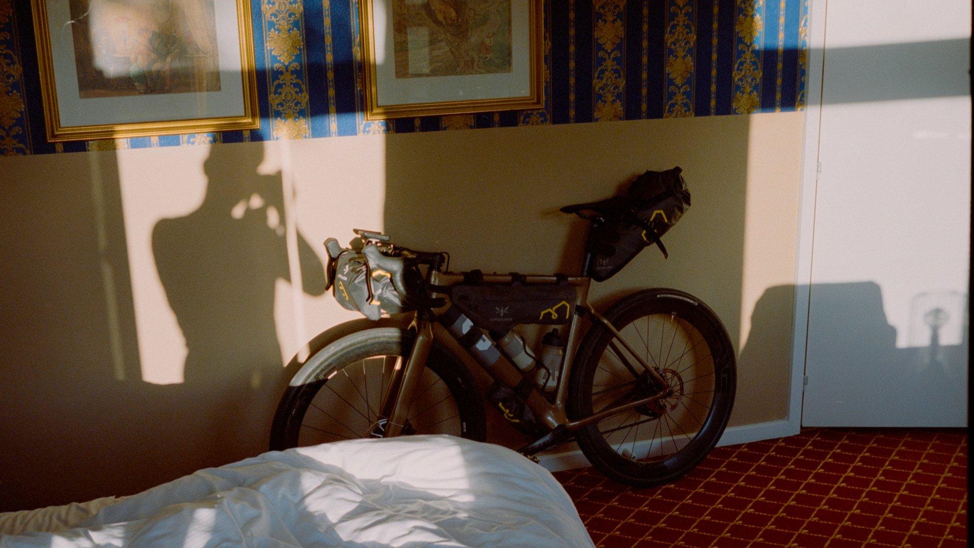 Dark road bike with bikepacking bags in hotel room with ornate wallpaper and framed artwork