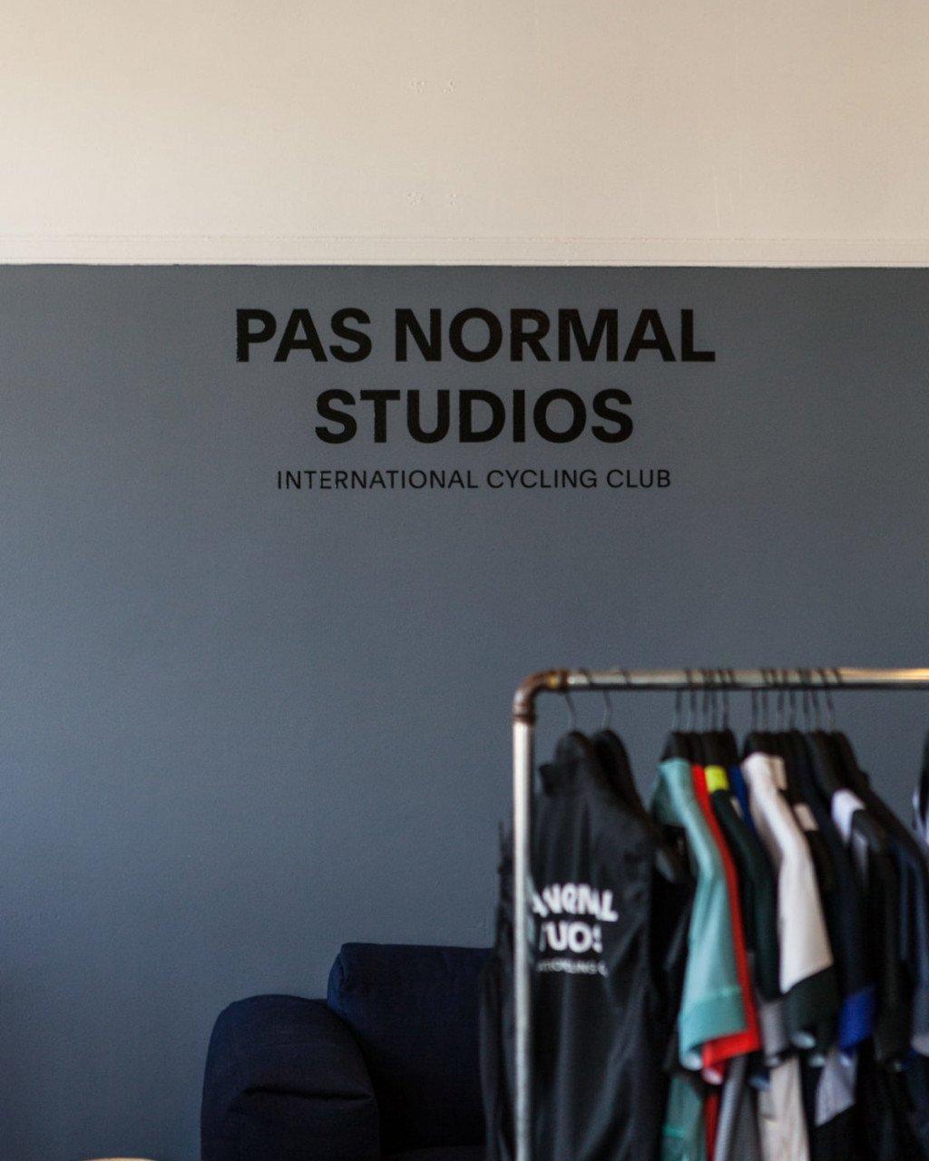 Cycling apparel hanging on clothing rack below brand logo and tagline on grey wall