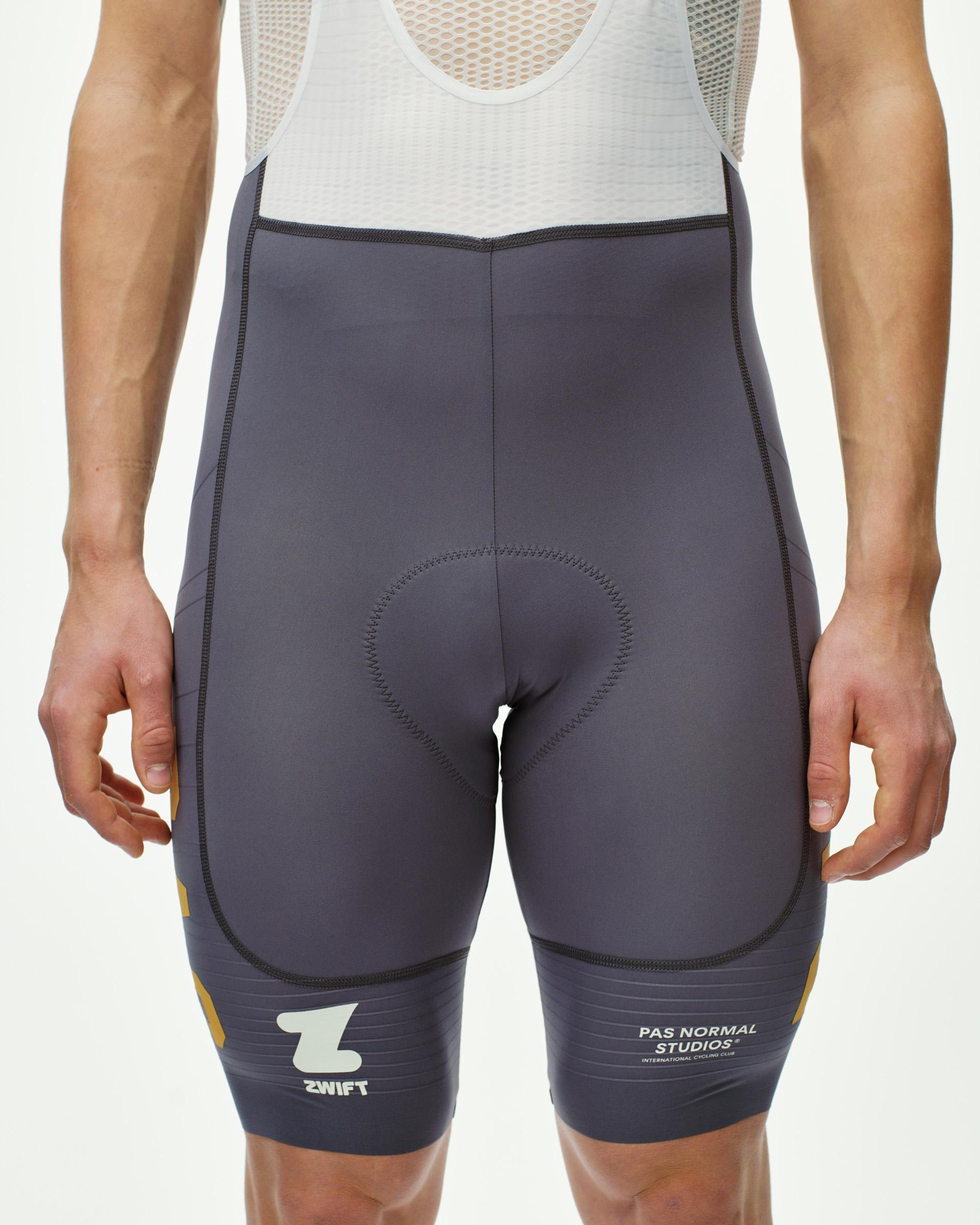 Grey Mechanism Pro PAS Racing cycling bibs on model, front view with gold Zwift logo at leg hem