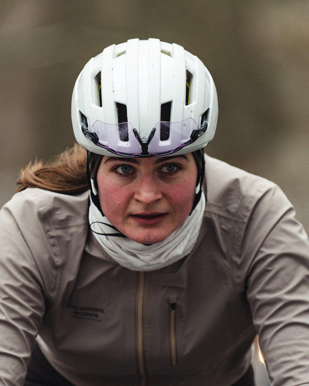 Model wearing white cycling helmet with purple accents and beige winter cycling jacket in racing position