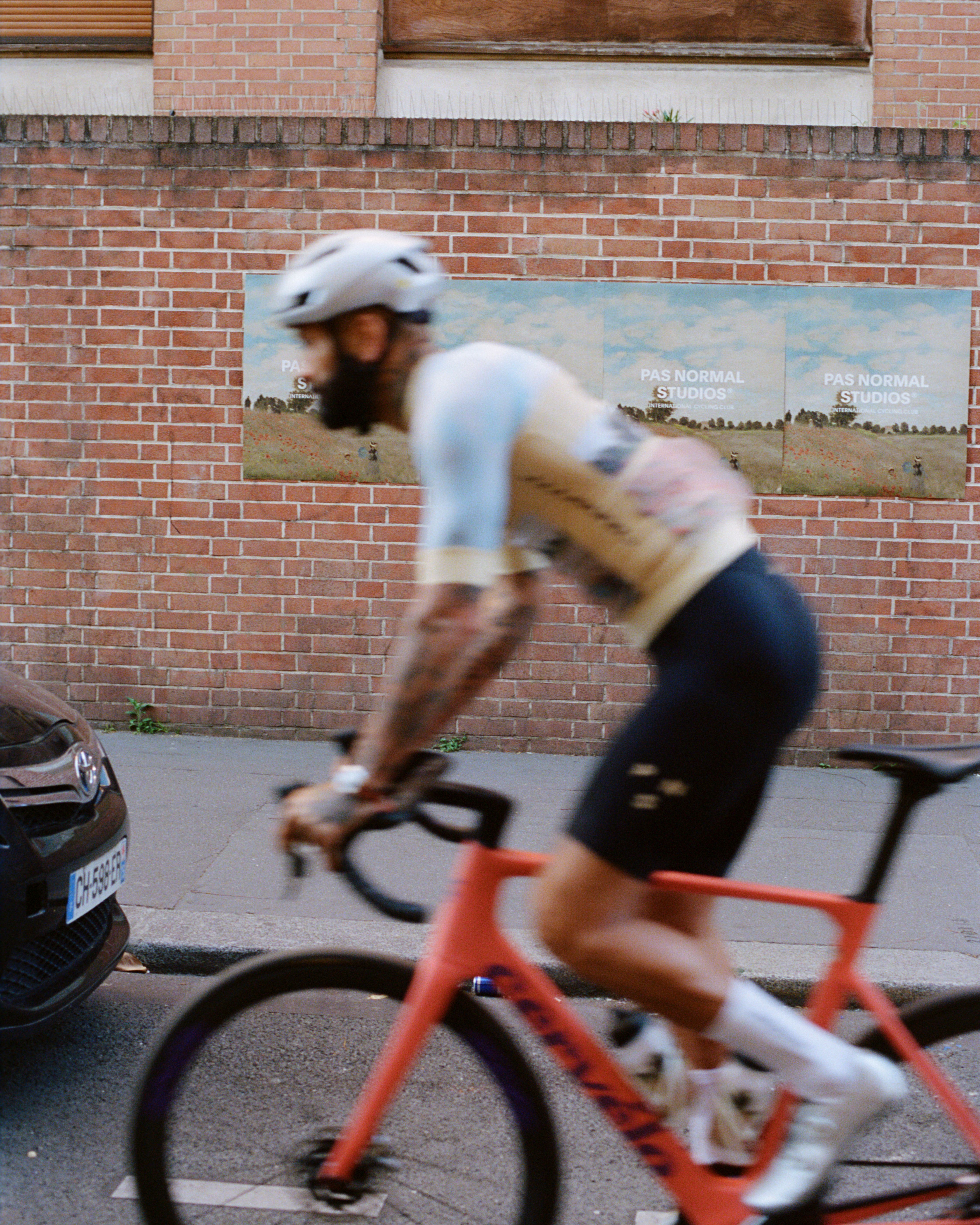 Cyclist in motion blur wearing white jersey and black shorts on orange bike past brick wall with campaign posters