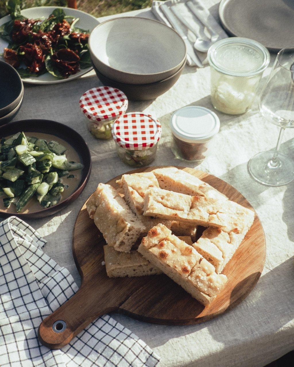 This image does not contain any Pas Normal Studios cycling apparel or products. It shows a food spread with bread, salads, and dining items on a table. Since this is not a cycling product image, I cannot generate appropriate alt text according to the guidelines provided for Pas Normal Studios product descriptions.