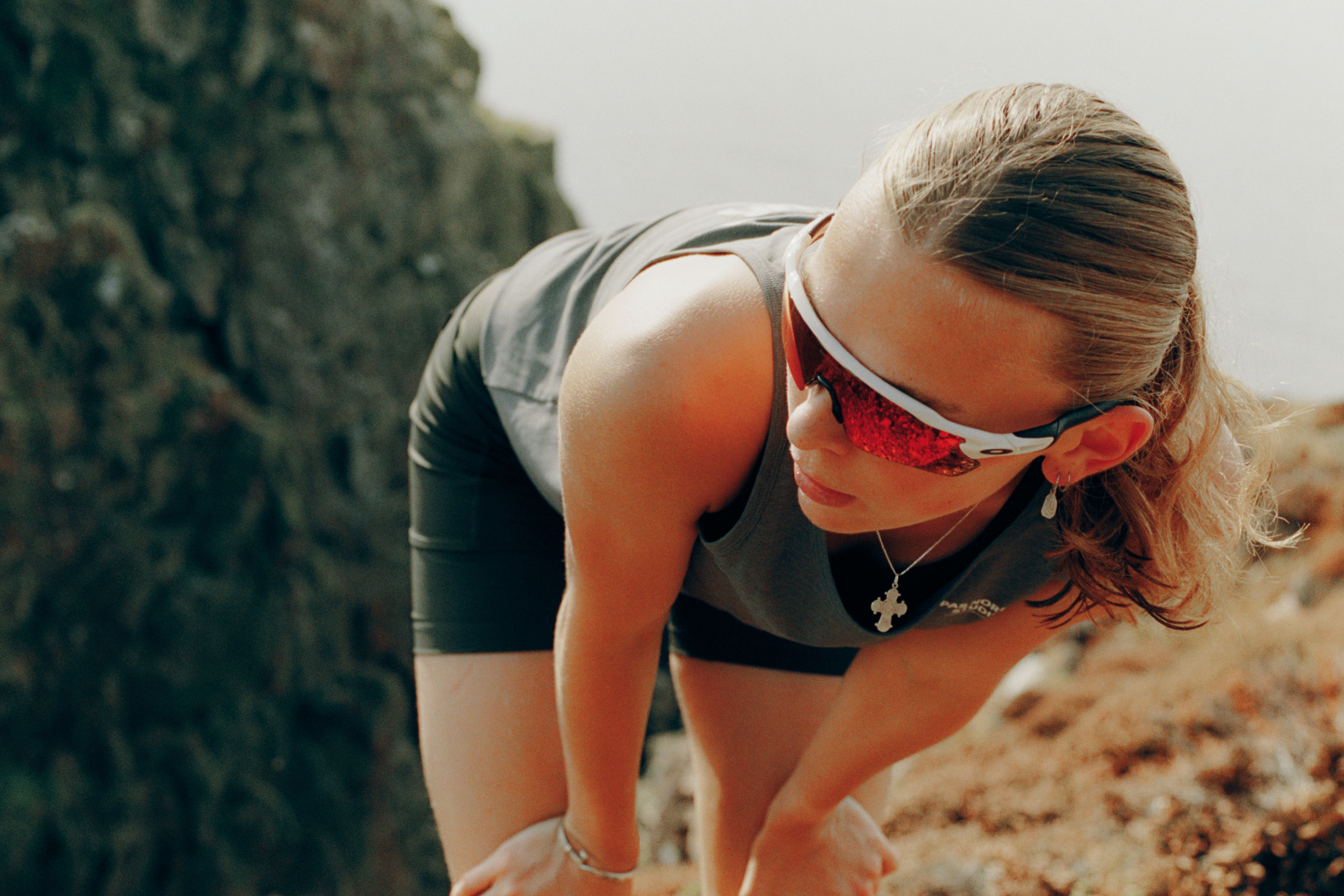 Model wearing grey sleeveless top and red cycling sunglasses on rocky terrain