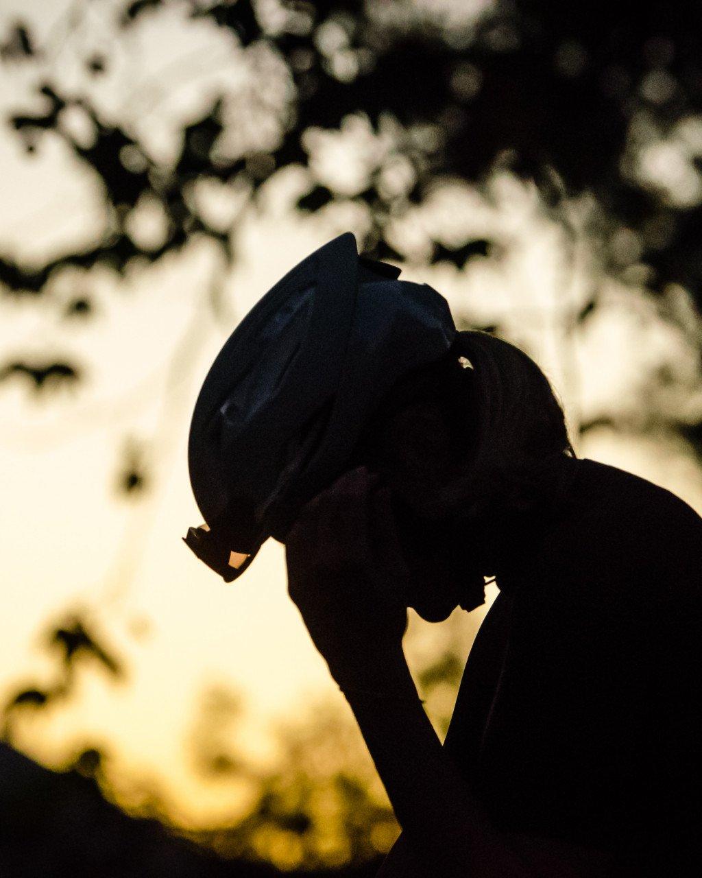 Cyclist silhouette adjusting helmet during golden hour lighting outdoors