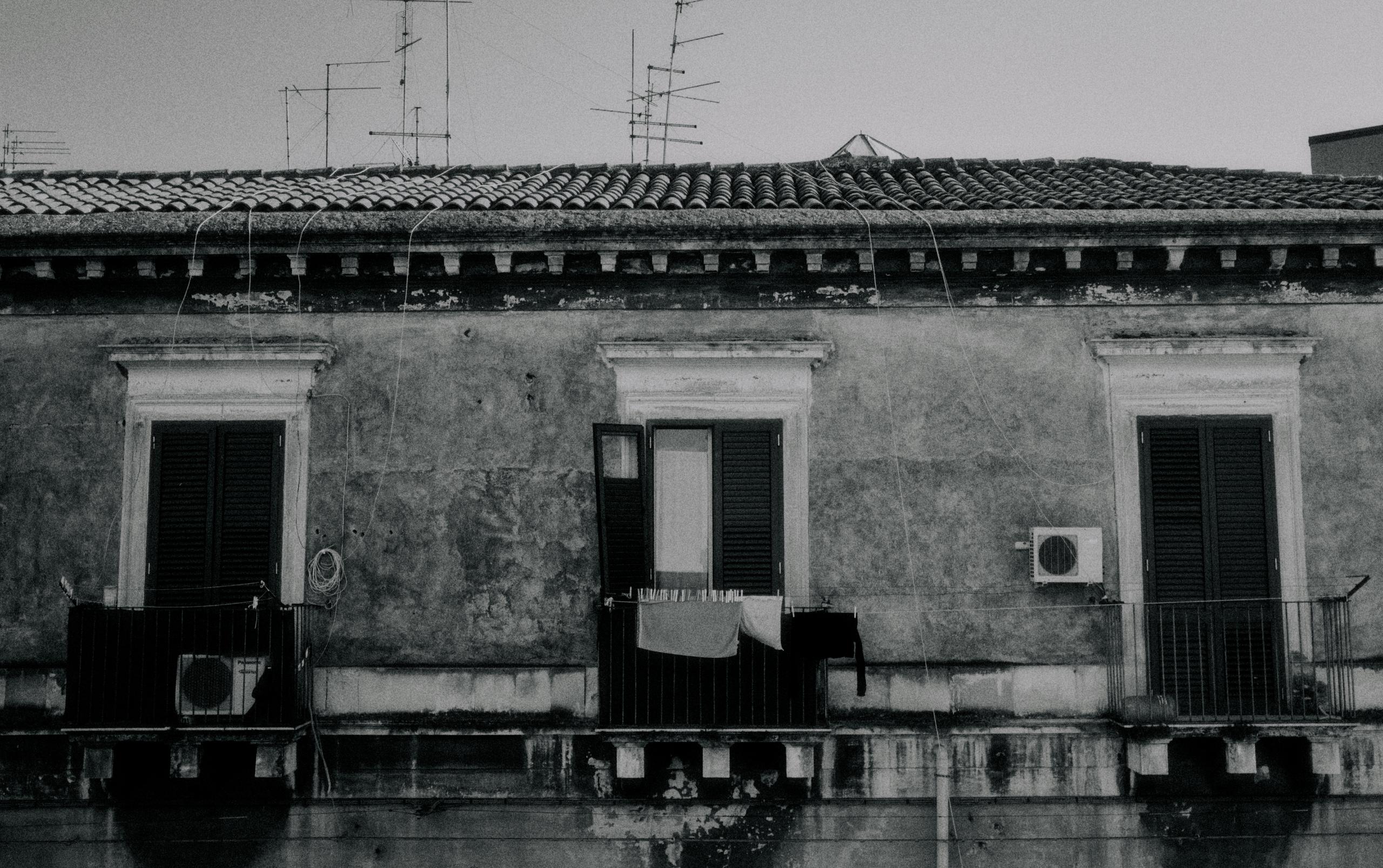 Black and white photograph of weathered Mediterranean building with traditional tile roof and balconies