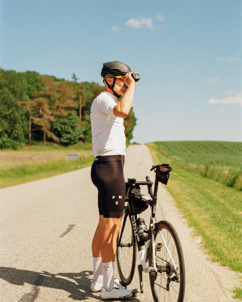 Model wearing white jersey and black cycling shorts with bike on countryside road