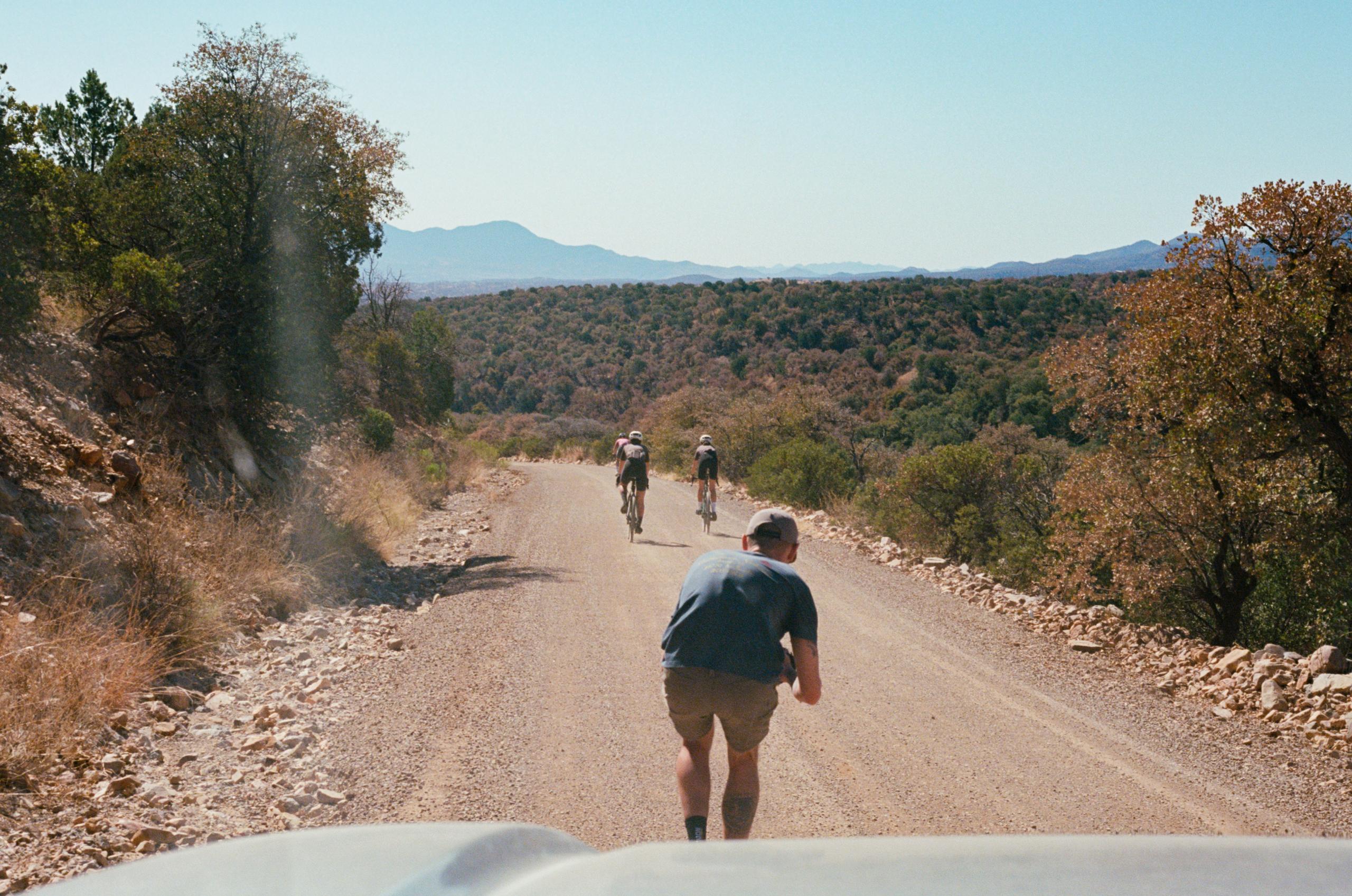 Cyclists training on gravel road through desert landscape with mountains in background