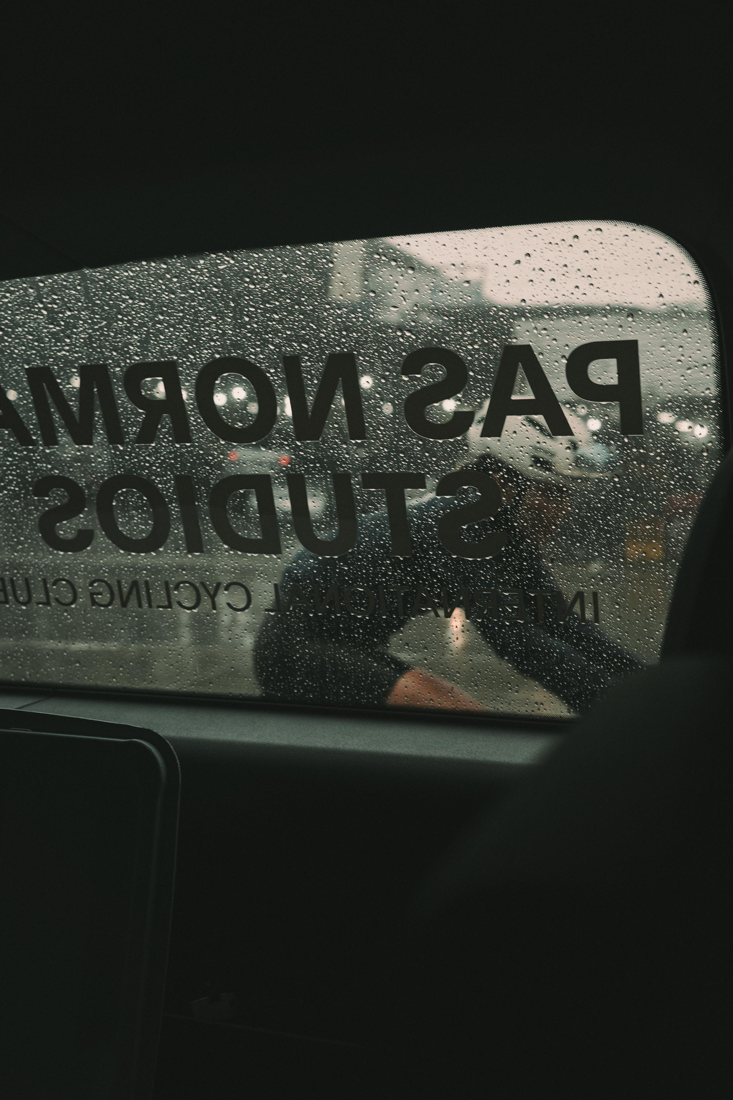 Rain-covered car window with reversed studio branding visible through glass