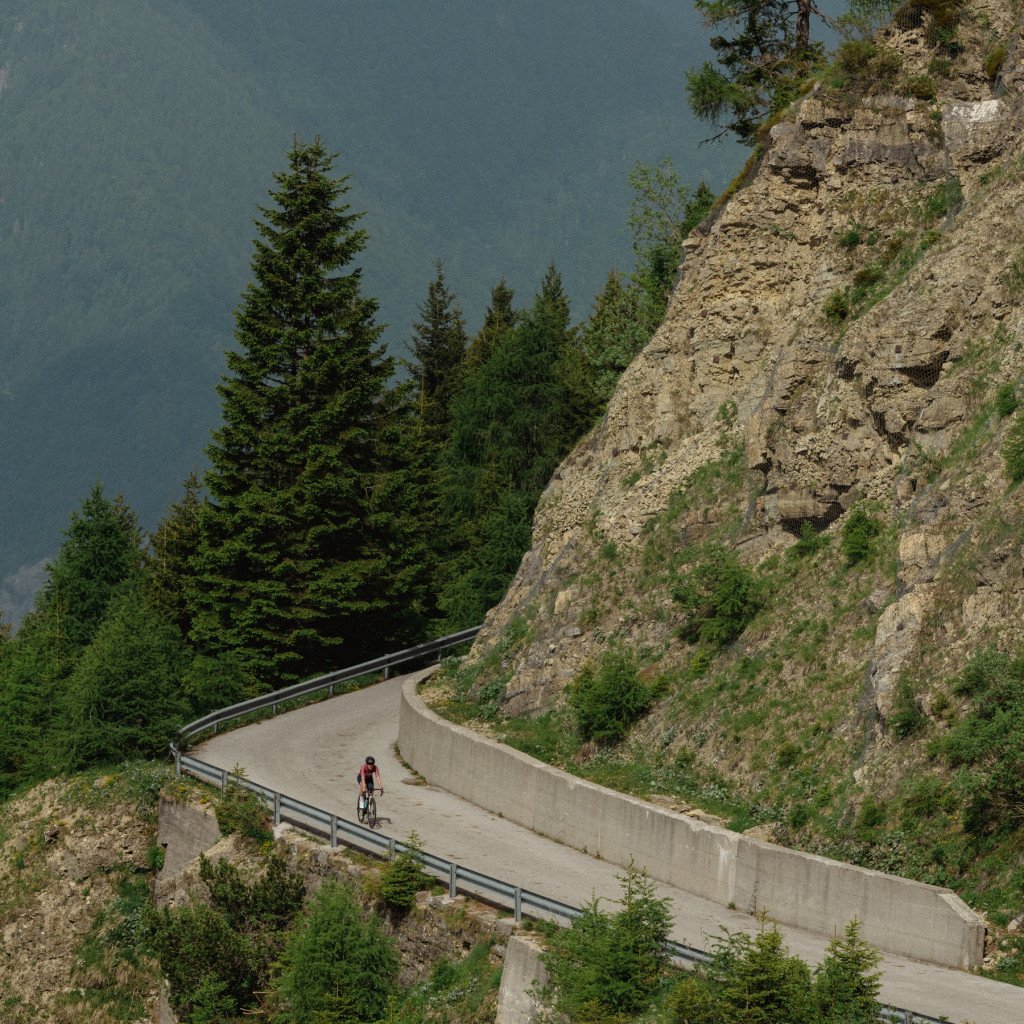 Cyclist in red jersey riding on winding mountain road through rocky terrain with evergreen trees