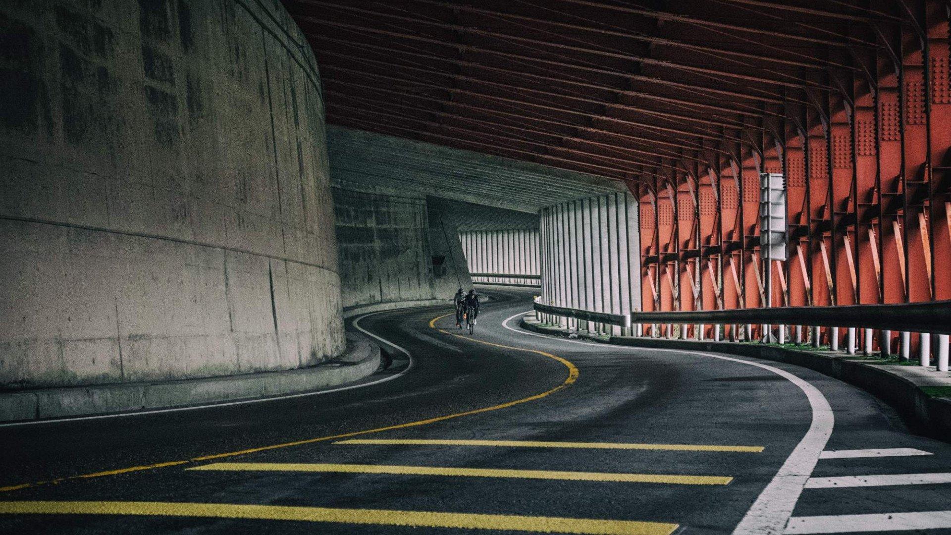 Cyclists riding through curved concrete tunnel with orange architectural details in Toyama, Japan