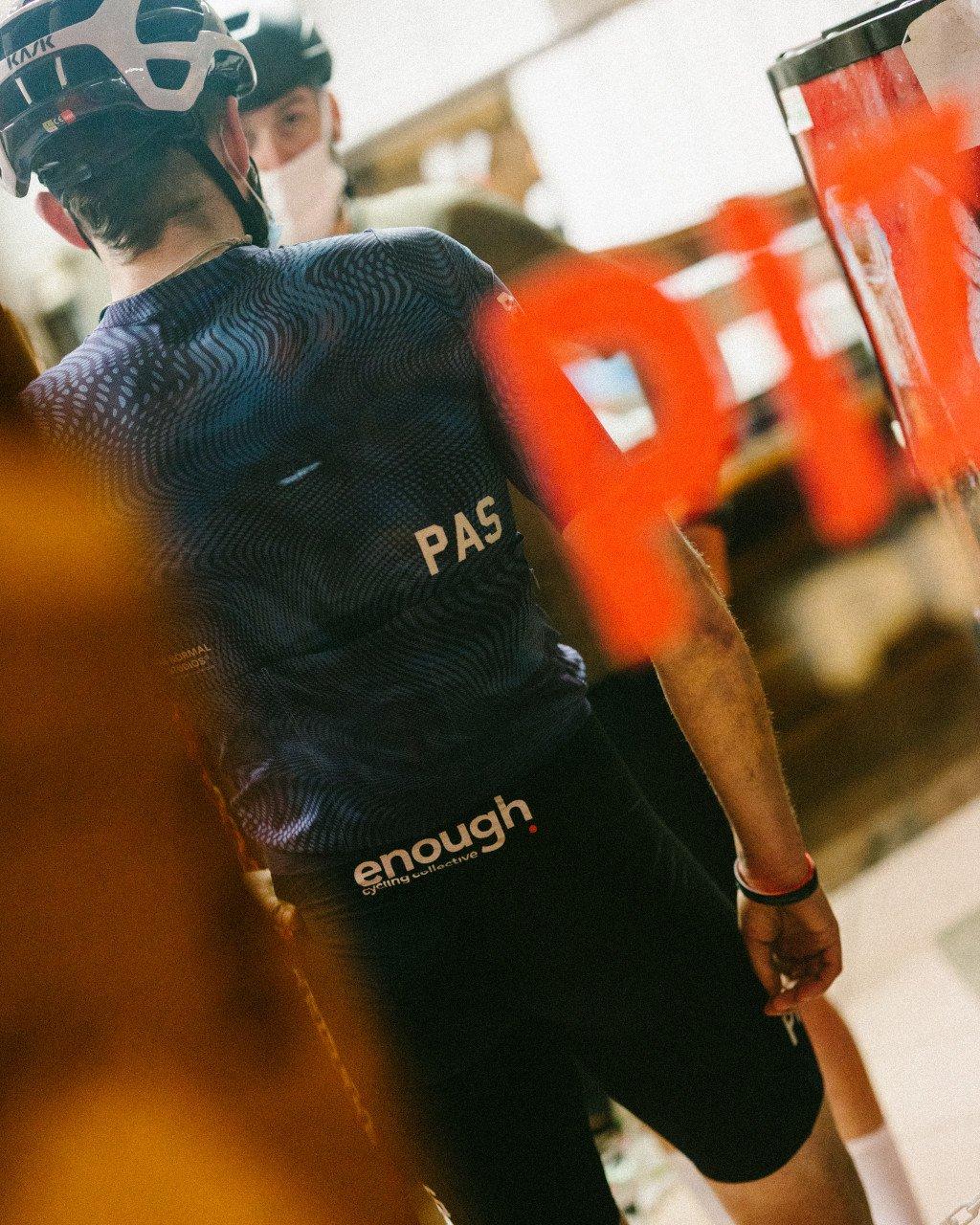 Model wearing black textured cycling jersey with PAS logo and enough. branding, positioned on stationary bike