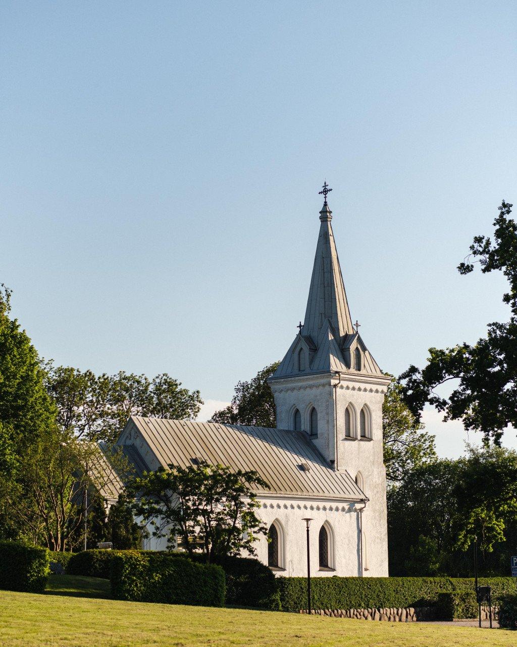 White church with spire surrounded by green trees and grass in Skåne countryside