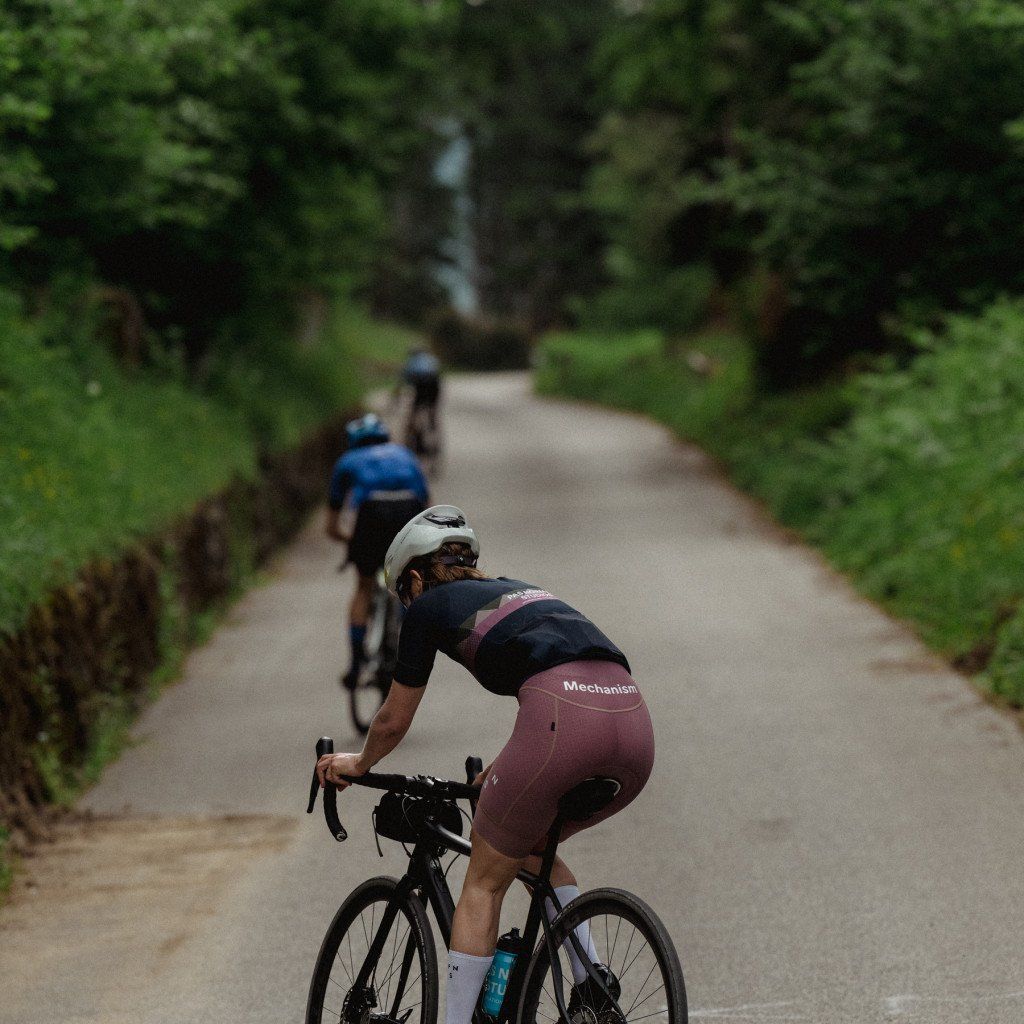 Cyclists riding on tree-lined road wearing Mechanism collection apparel in aerodynamic position