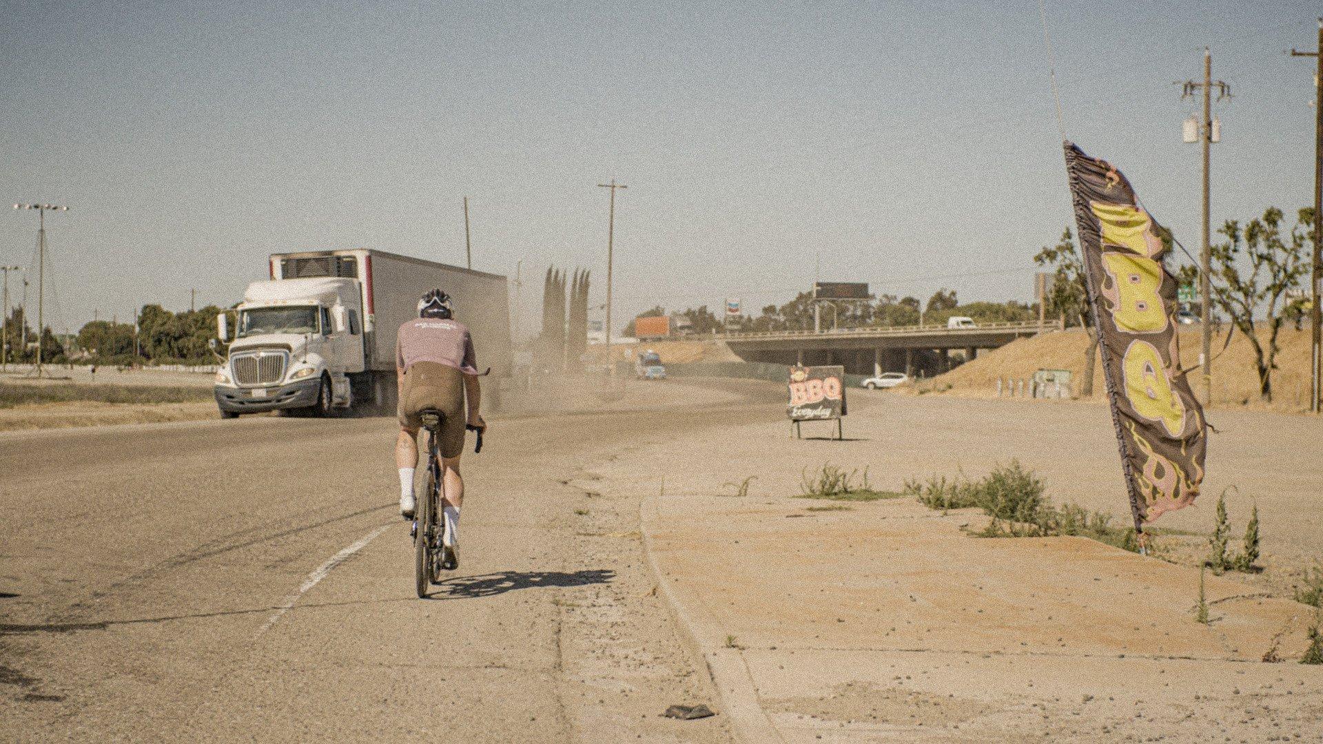 Cyclist in aerodynamic position on desert highway with truck and roadside signage