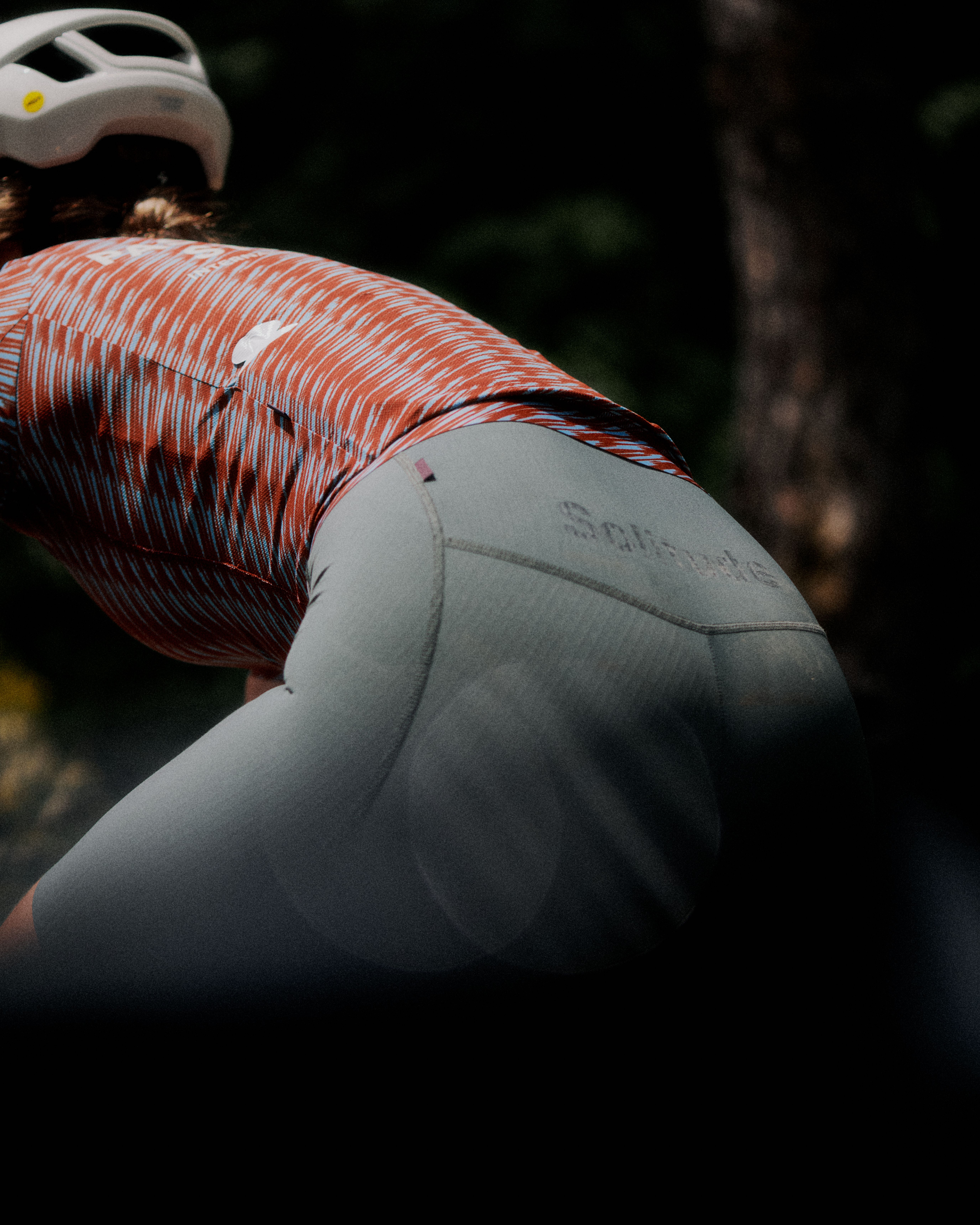 Model wearing orange and white striped jersey with grey cycling shorts in riding position