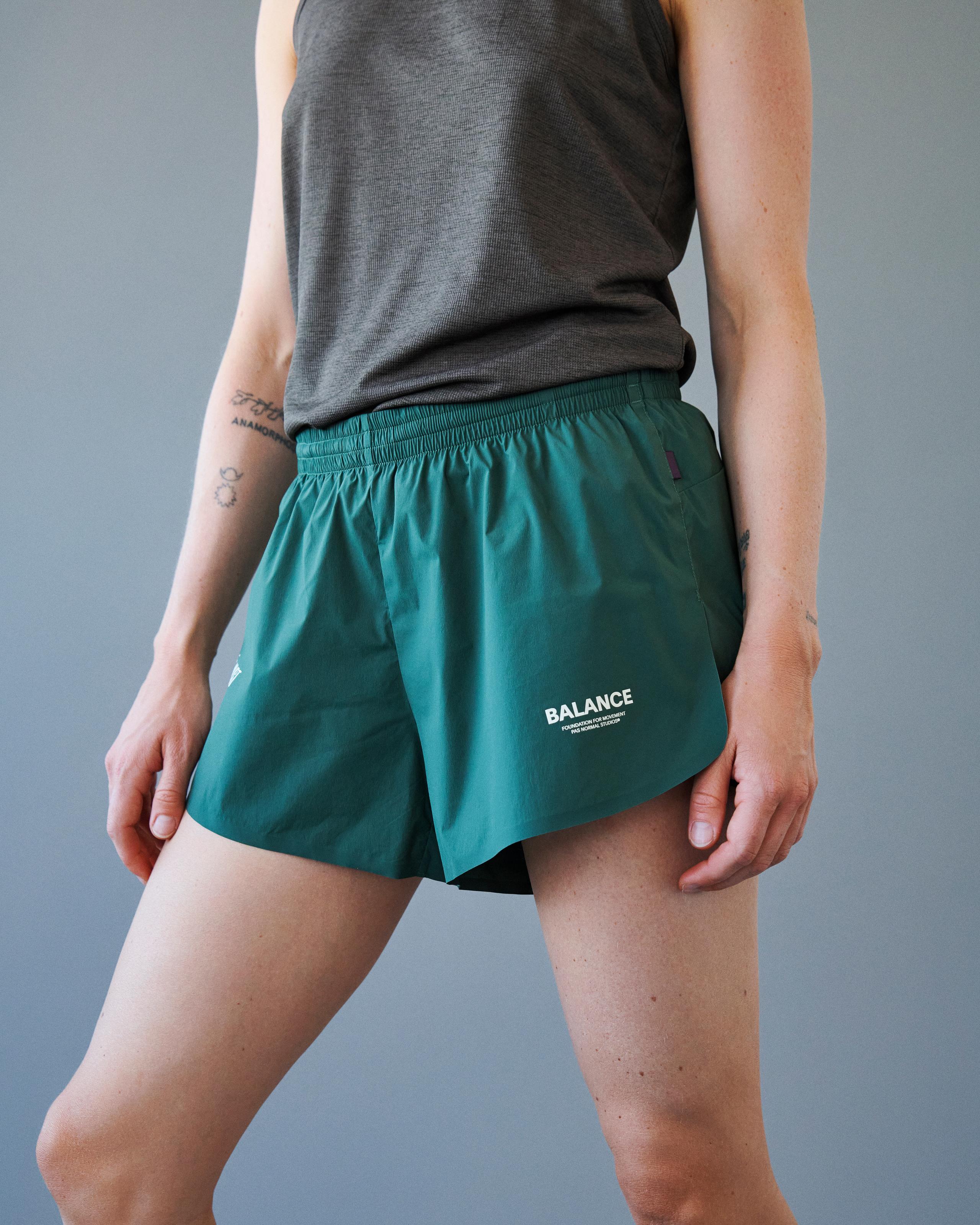 Forest Green Balance shorts on model, front three-quarter view with elastic waistband and white chest logo print
