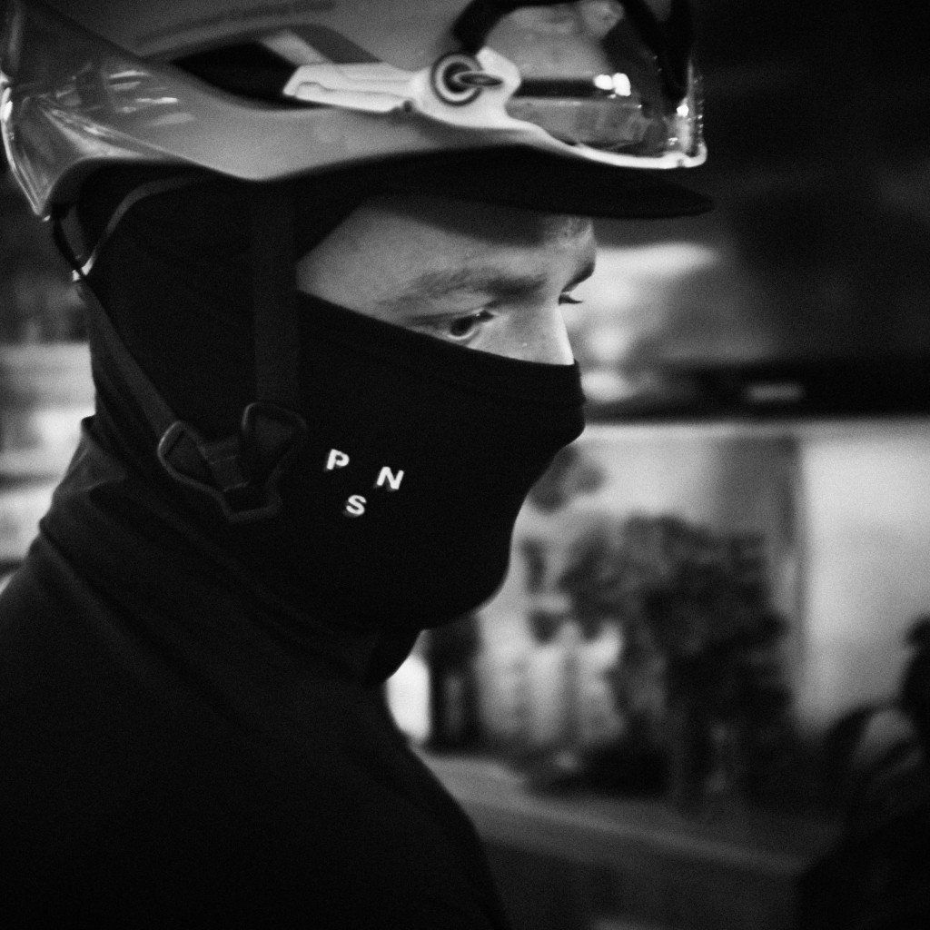 Model wearing black balaclava with logo lettering and protective eyewear in black and white