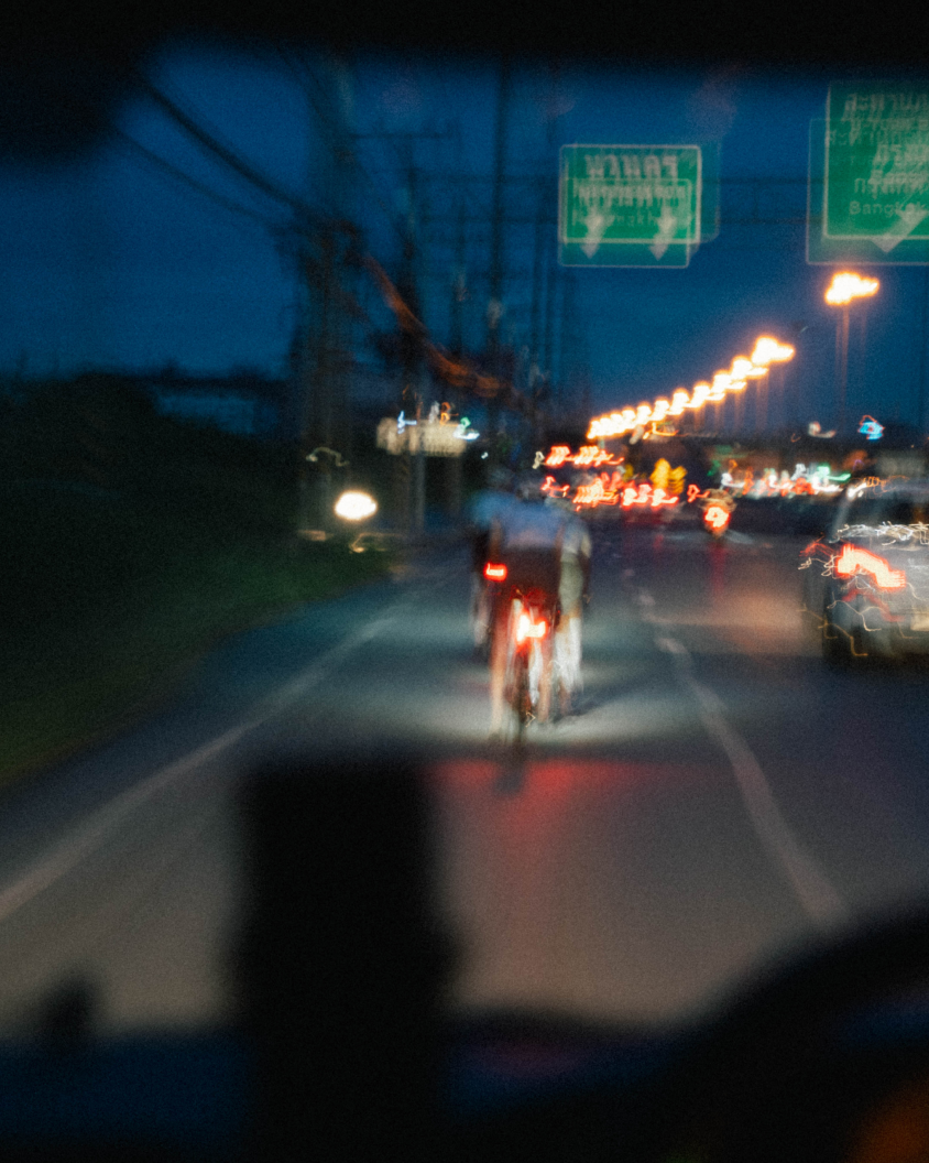 Cyclist with rear light riding on city street at dusk with traffic and streetlights