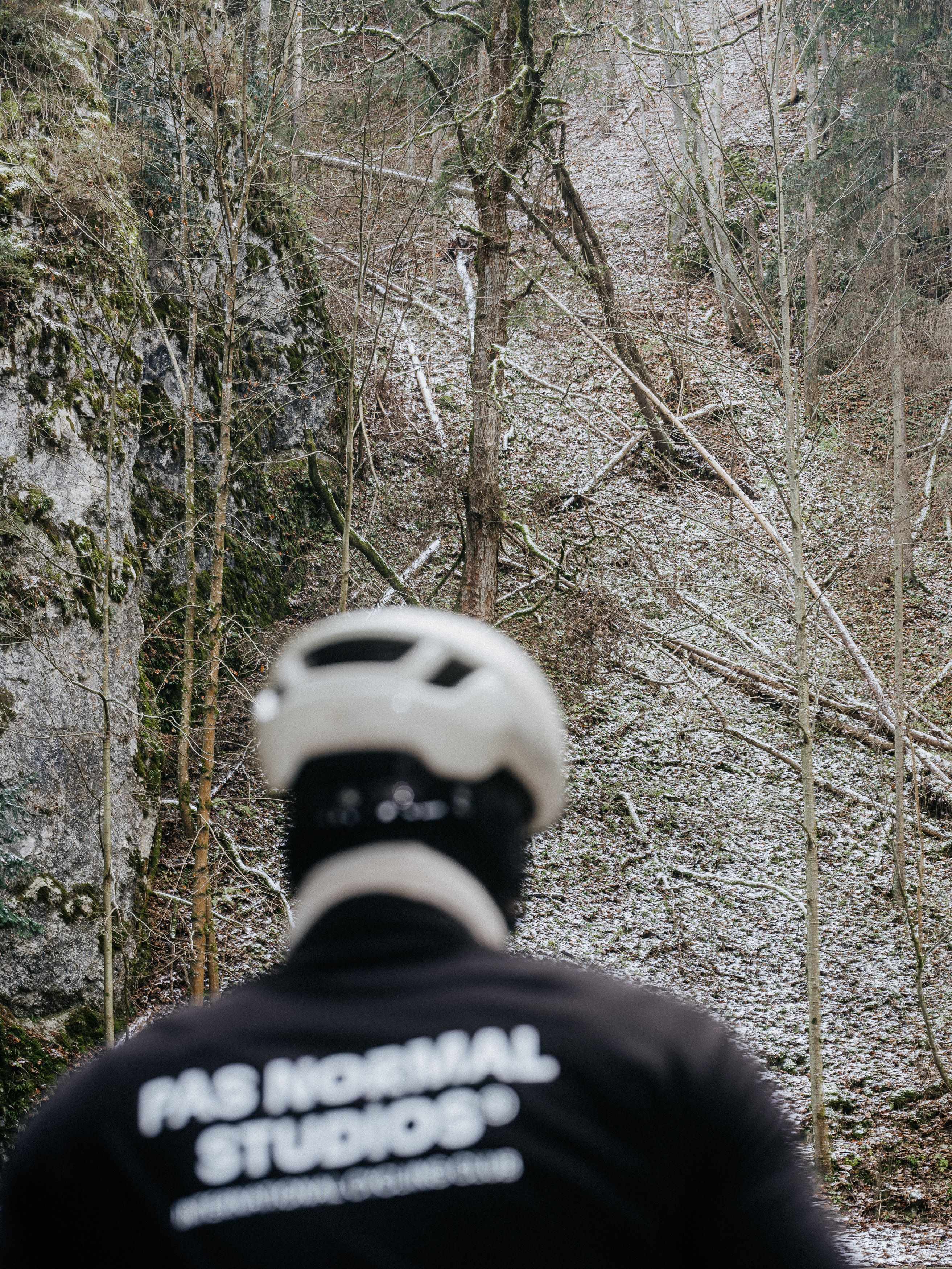 Cyclist wearing dark jacket with white logo text riding on rocky forest trail