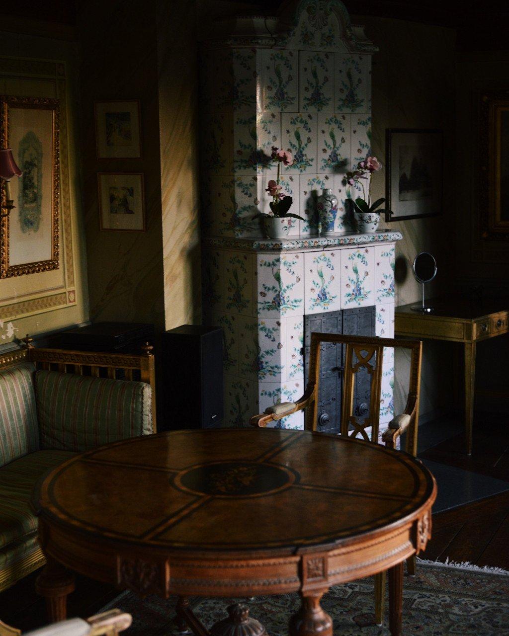 Elegant interior room with floral wallpaper, ornate furniture, and traditional fireplace in warm natural light