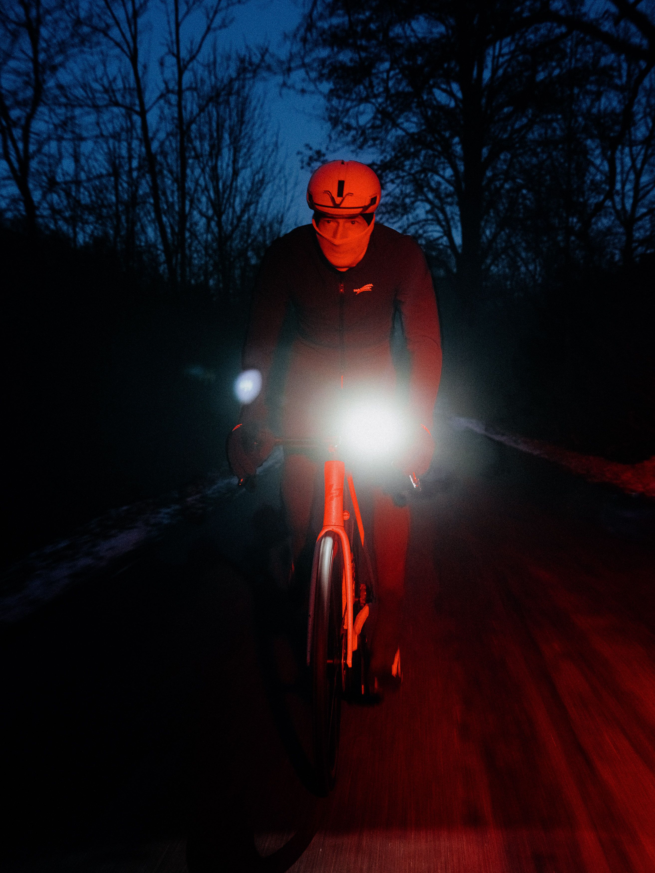 Cyclist riding through forest at dusk with bright bike lights illuminating the path