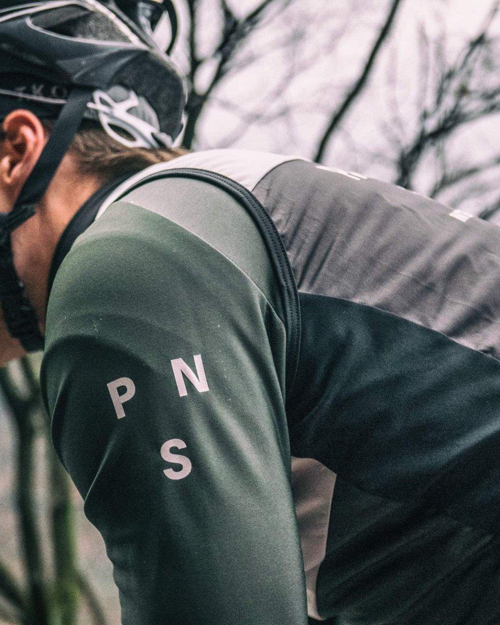 Model wearing green jersey with white lettering on sleeve, cycling helmet, with backpack in outdoor setting