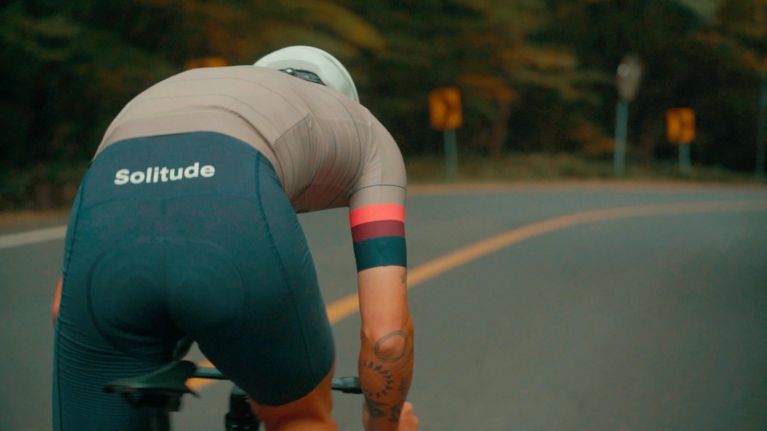 Model wearing Solitude collection green cycling jersey with tan sleeves and striped armband, cycling on road