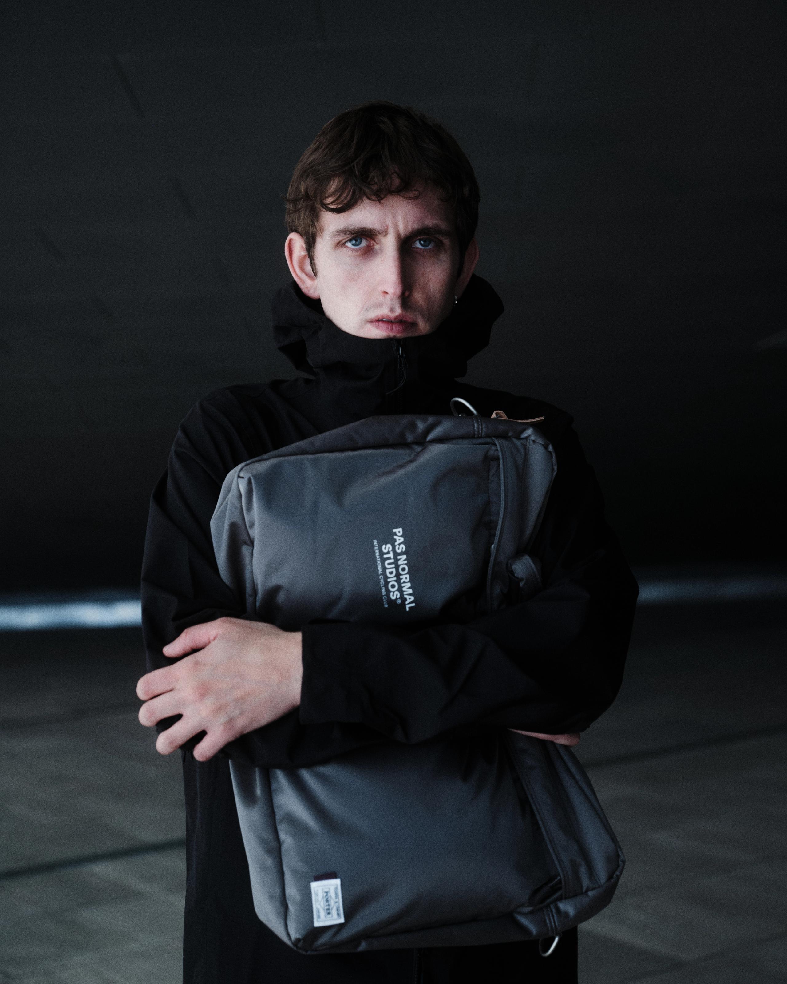 Model wearing black hoodie holding grey Porter collaboration bag with logo text