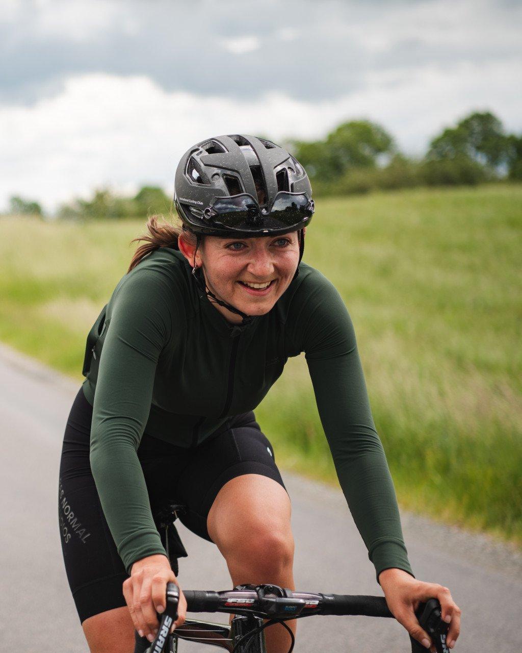 Model wearing green long sleeve jersey in aerodynamic position on bike in countryside setting