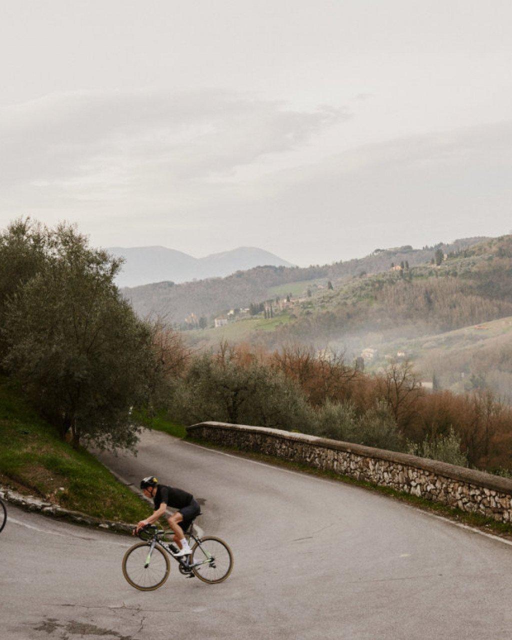 Cyclist in dark kit riding on winding mountain road through Italian countryside