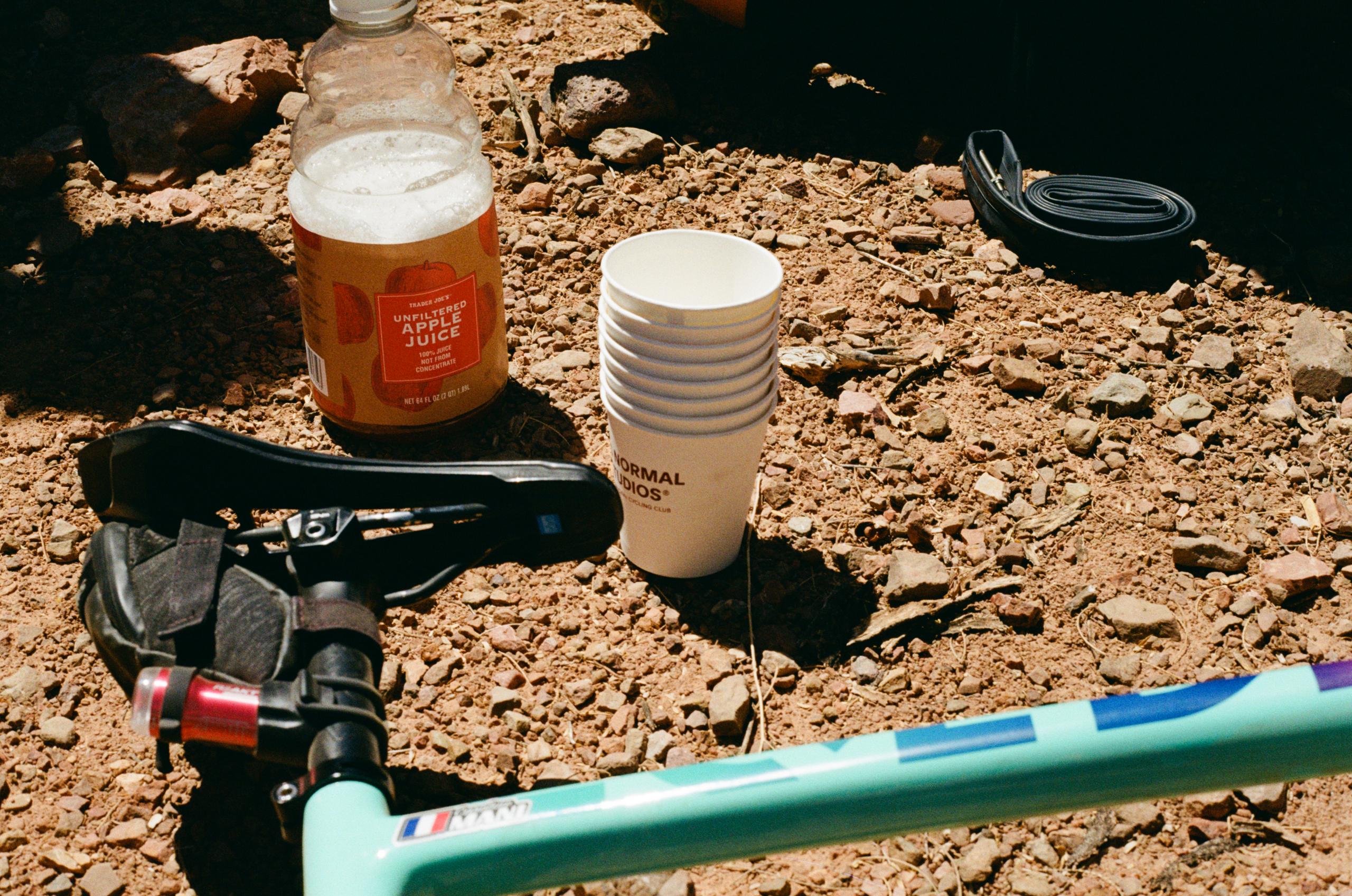 Cycling accessories and refreshments arranged on desert ground including bike pump, water bottle, and cups