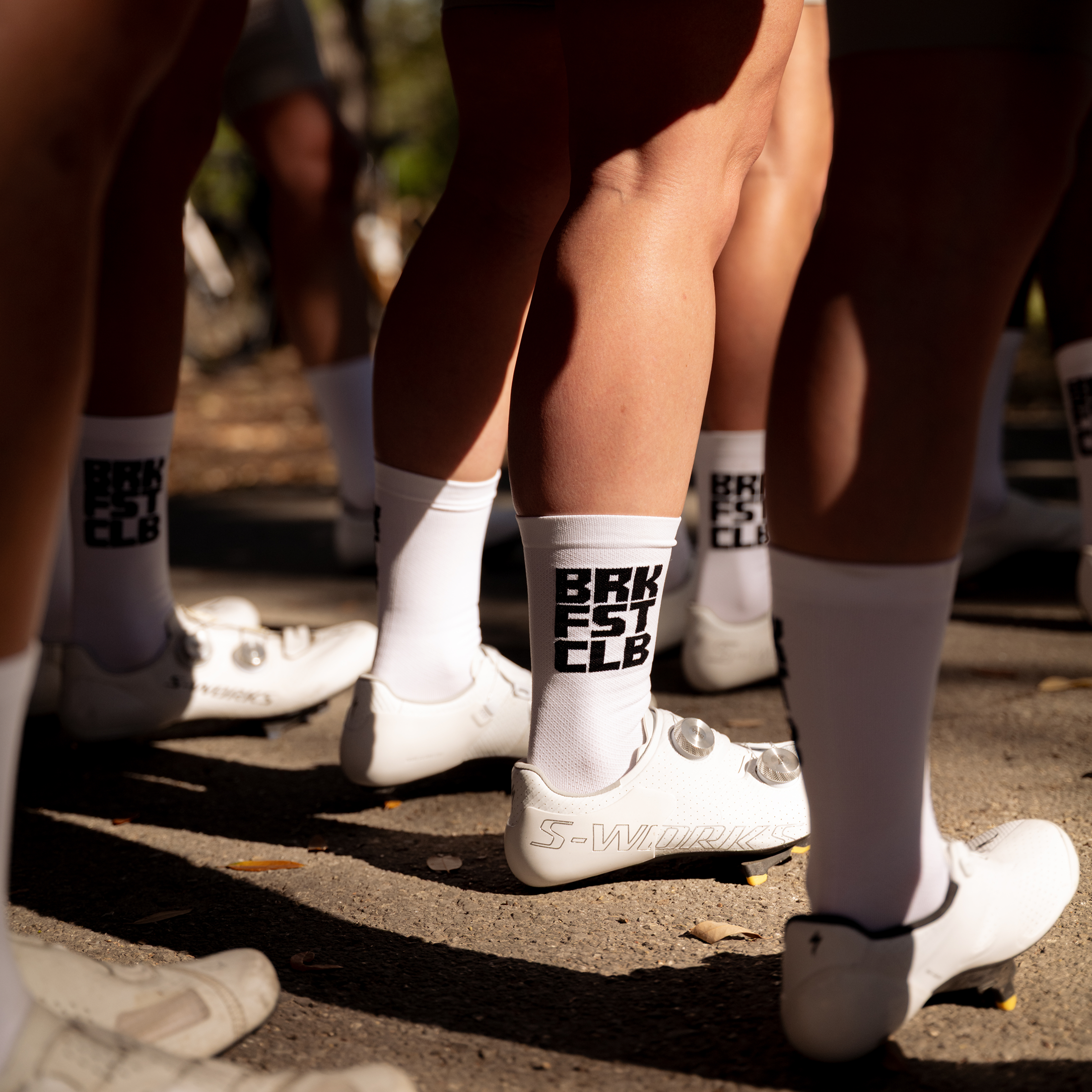 White cycling socks with black lettering worn by cyclists in sunlight