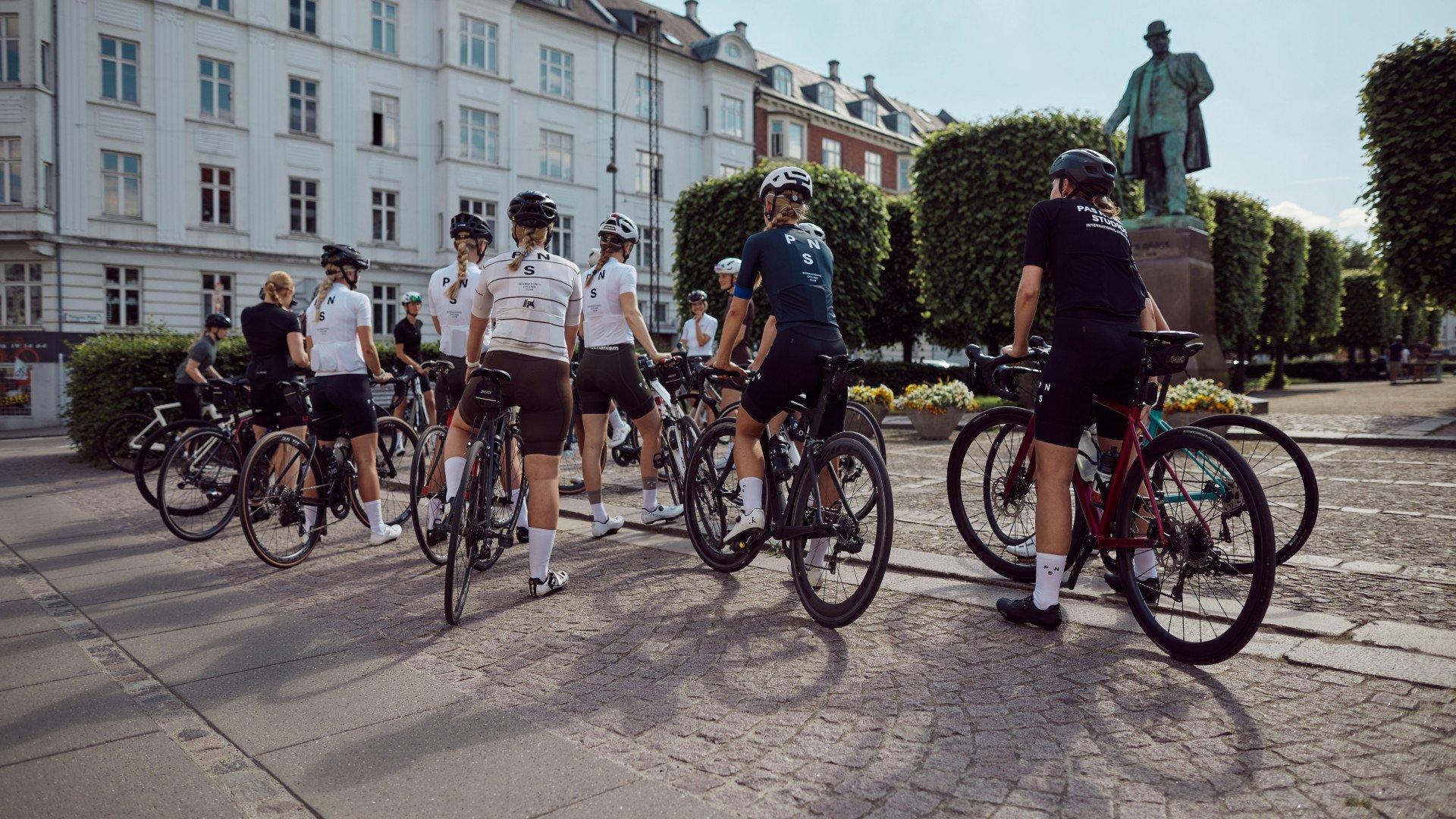 Group of cyclists with bikes in white and navy cycling apparel gathered in cobblestone square