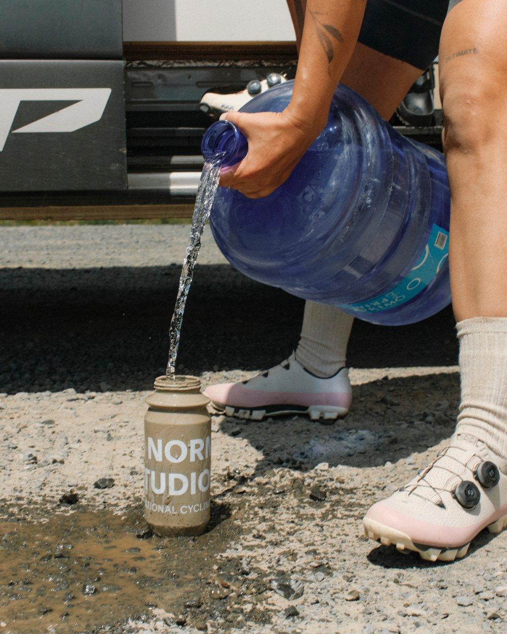 Cyclist pouring water from blue bottle into recovery drink container after ride