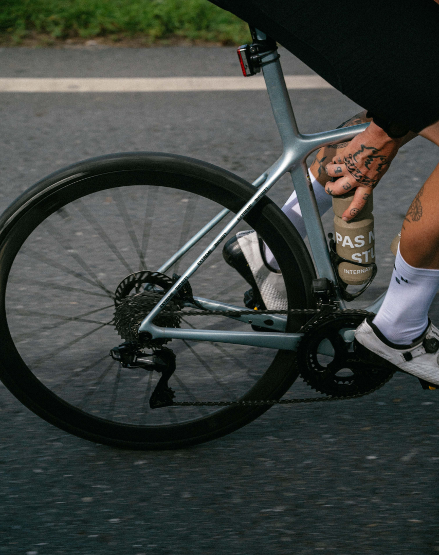 Model on road bike wearing white cycling socks and black shorts, close-up of tattooed hands and bike frame