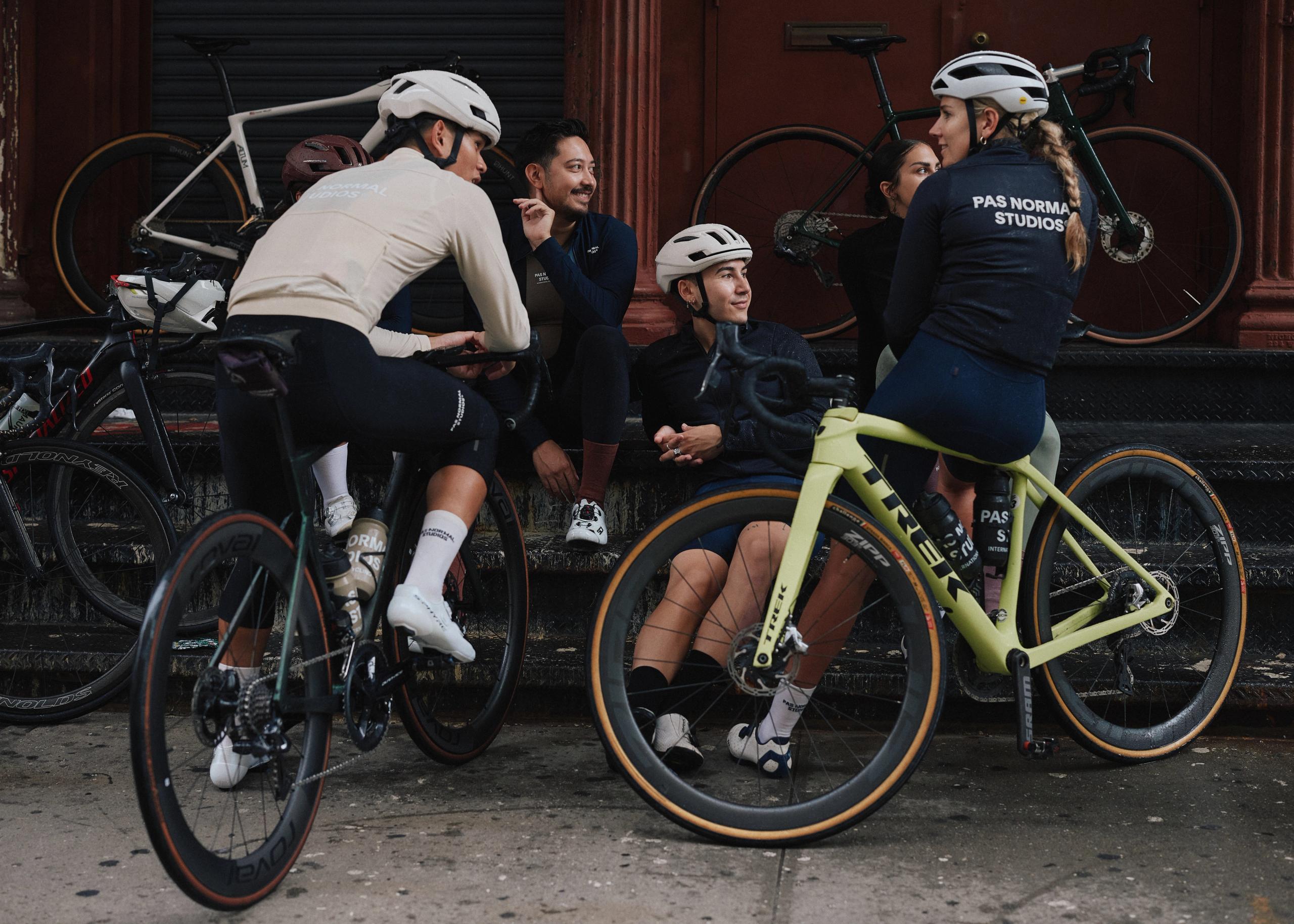 Group of cyclists socializing with bikes, wearing navy and cream cycling apparel with logo branding