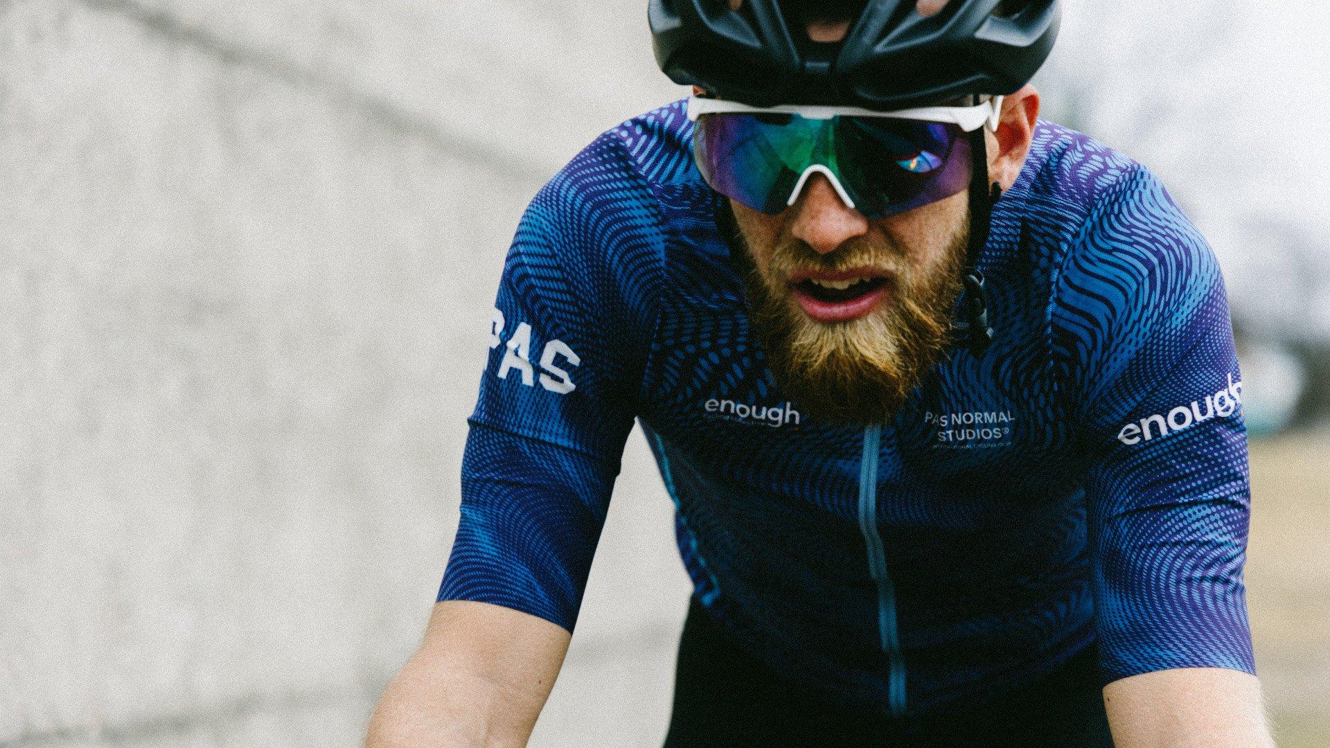 Model wearing blue PAS collection cycling jersey with geometric pattern and sponsor branding during race