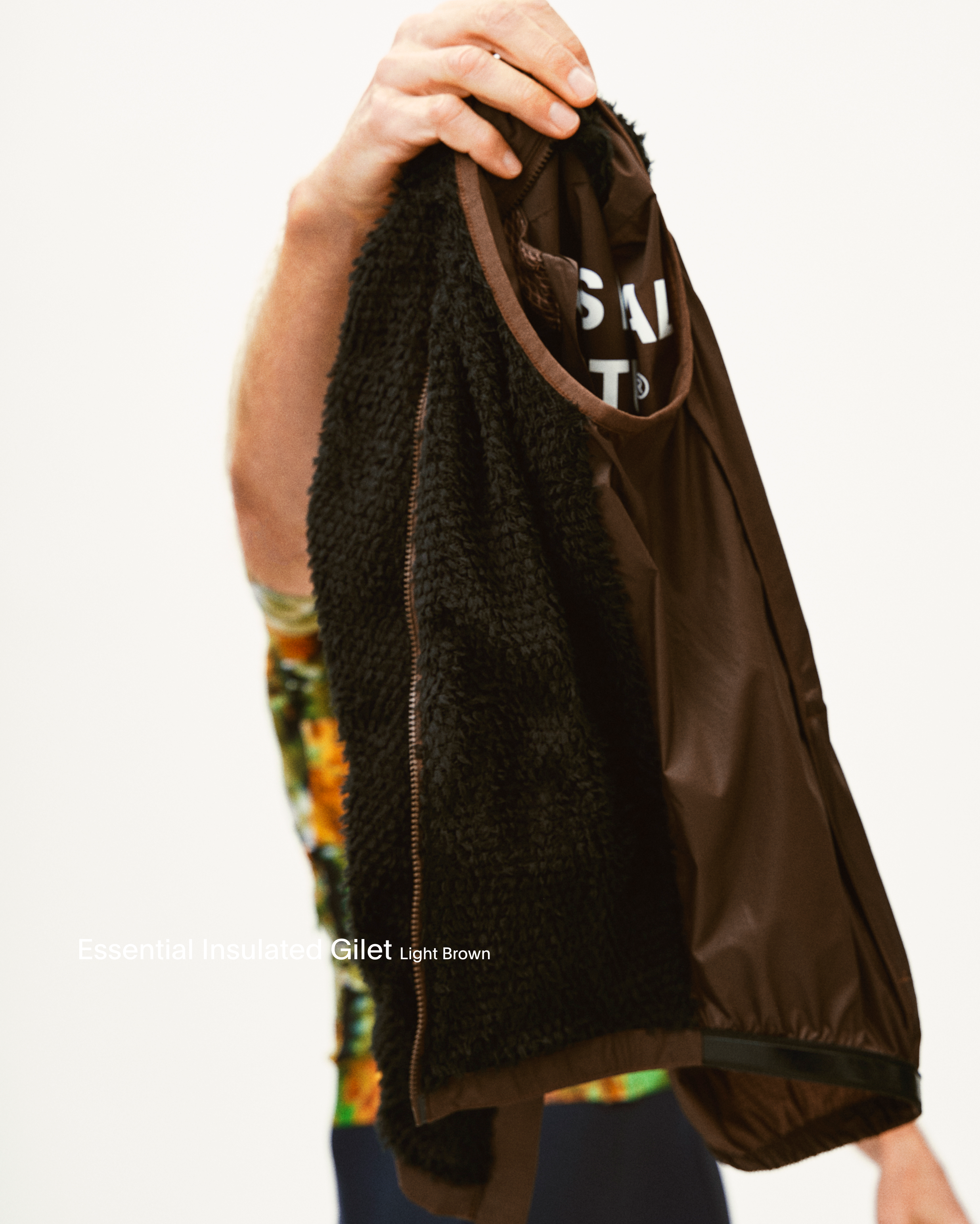Model holding brown Gilet with textured panel and chest logo