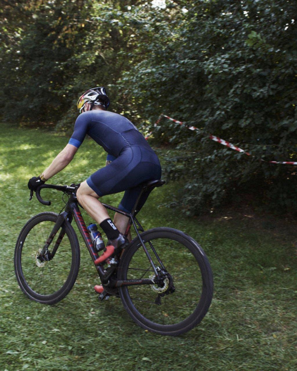 Model wearing navy blue cycling skinsuit on mountain bike in wooded setting