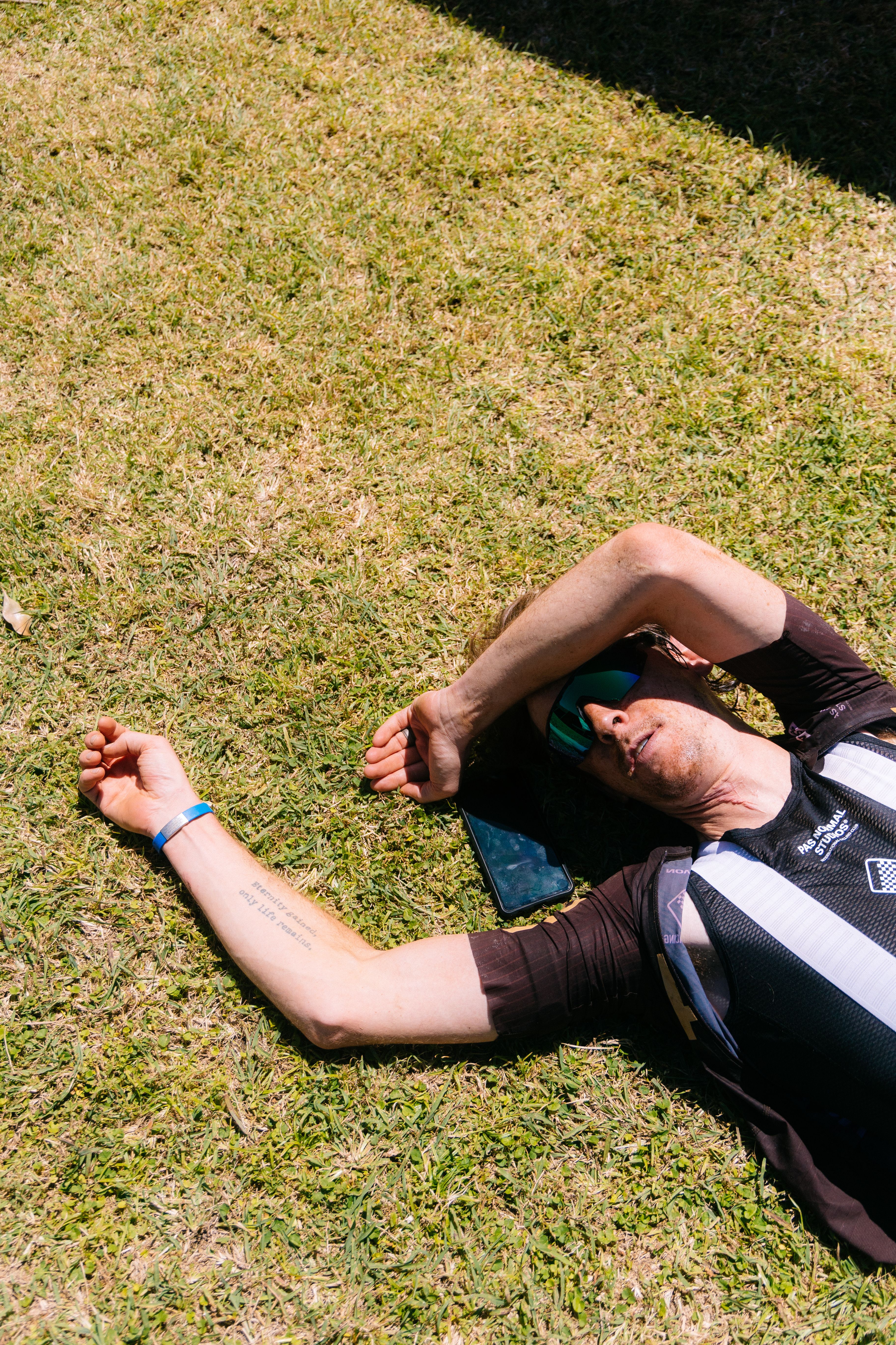 Model wearing dark cycling jersey lying on grass with arms raised and phone beside him