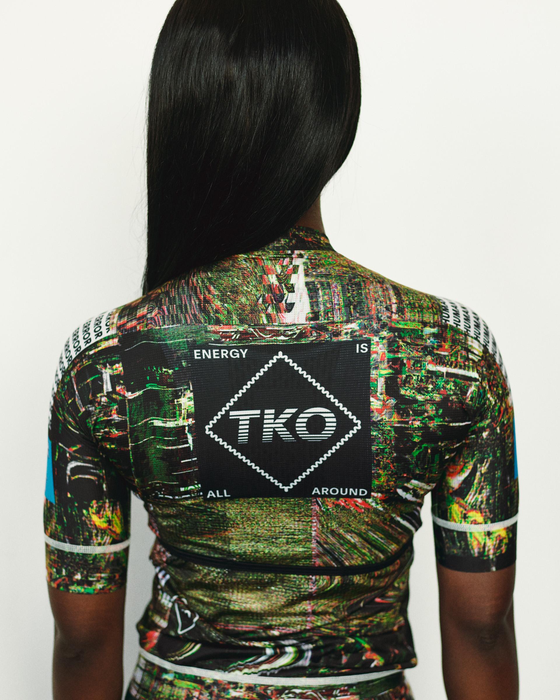 Human Error Green T.K.O. Mechanism women's cycling jersey on model, rear view with glitch-print AOP and TKO back panel