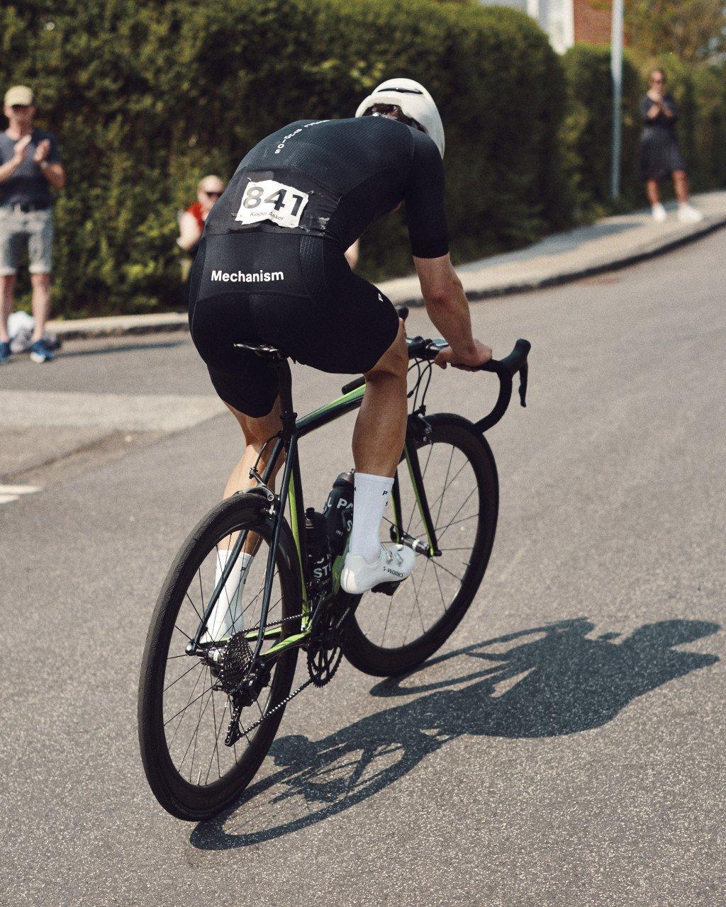 Model wearing black Mechanism cycling kit in aerodynamic position during time trial race
